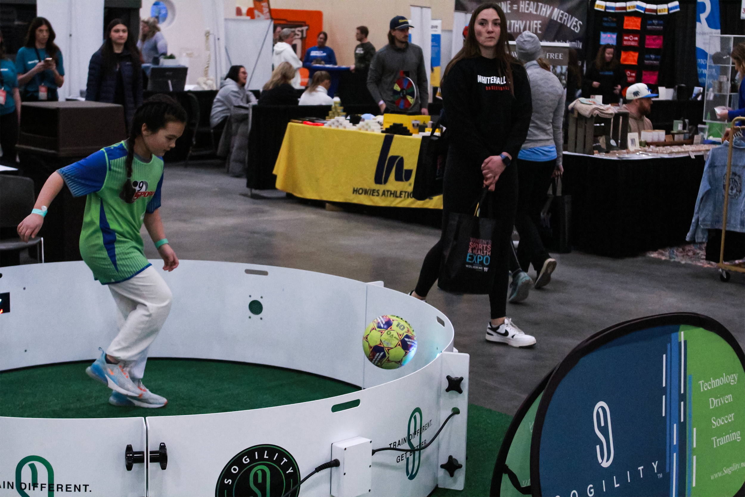 A young girl in a sports jersey playing soccer using an interactive system at the Women's Sports & Health  expo.