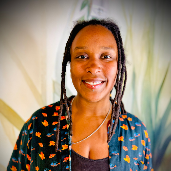 Portrait of a woman with glasses and short natural hair, wearing a light-colored button-up shirt, against a dark background.