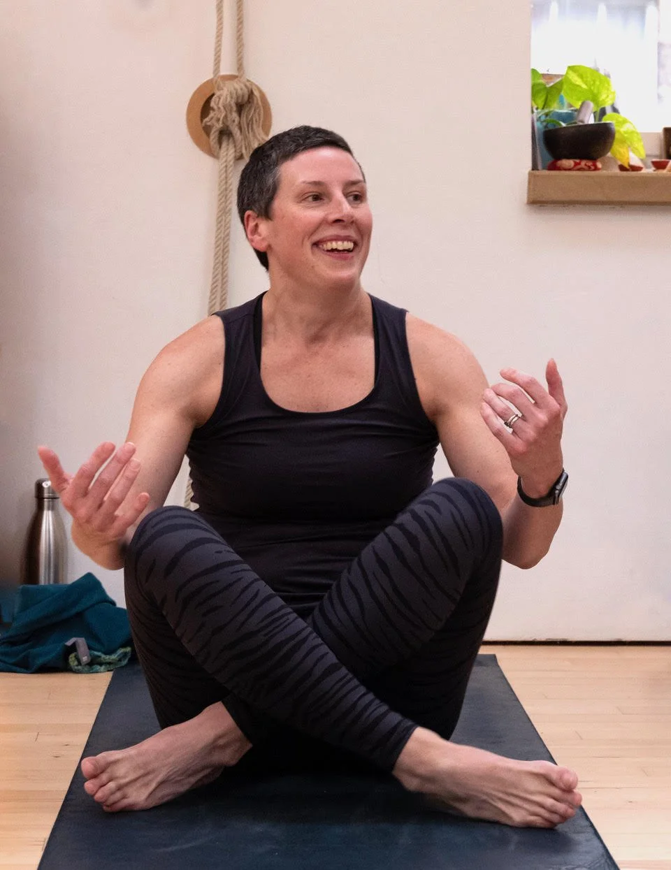 A man practicing yoga in a seated spinal twist pose on a yoga mat in a room with a rope wall.