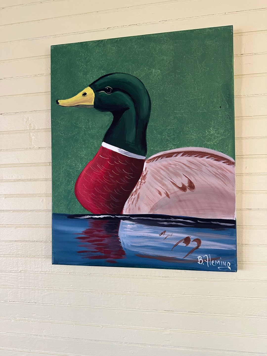 A framed painting of a mallard duck by artist Barbara Fleming, displayed on a bright yellow wall