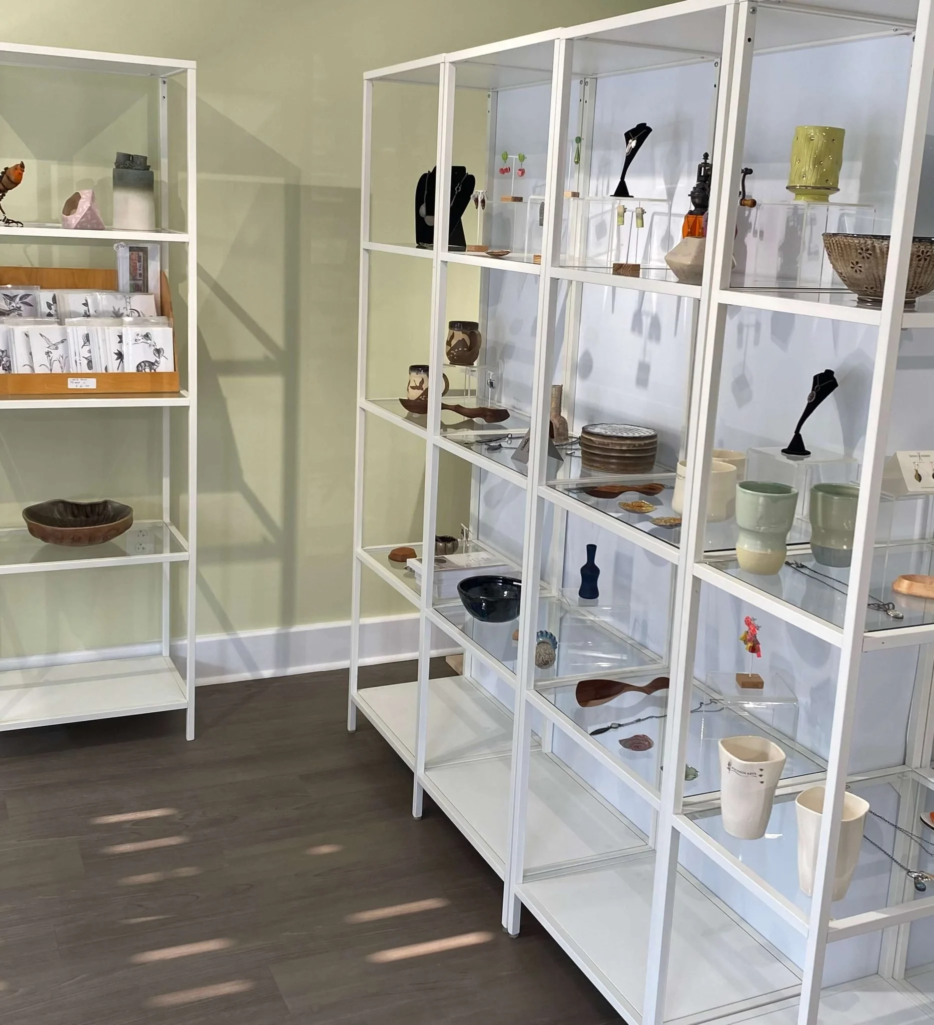 Display shelves in a gallery showcasing ceramic pottery and handmade crafts. Items are arranged neatly, creating an organized and artistic atmosphere.