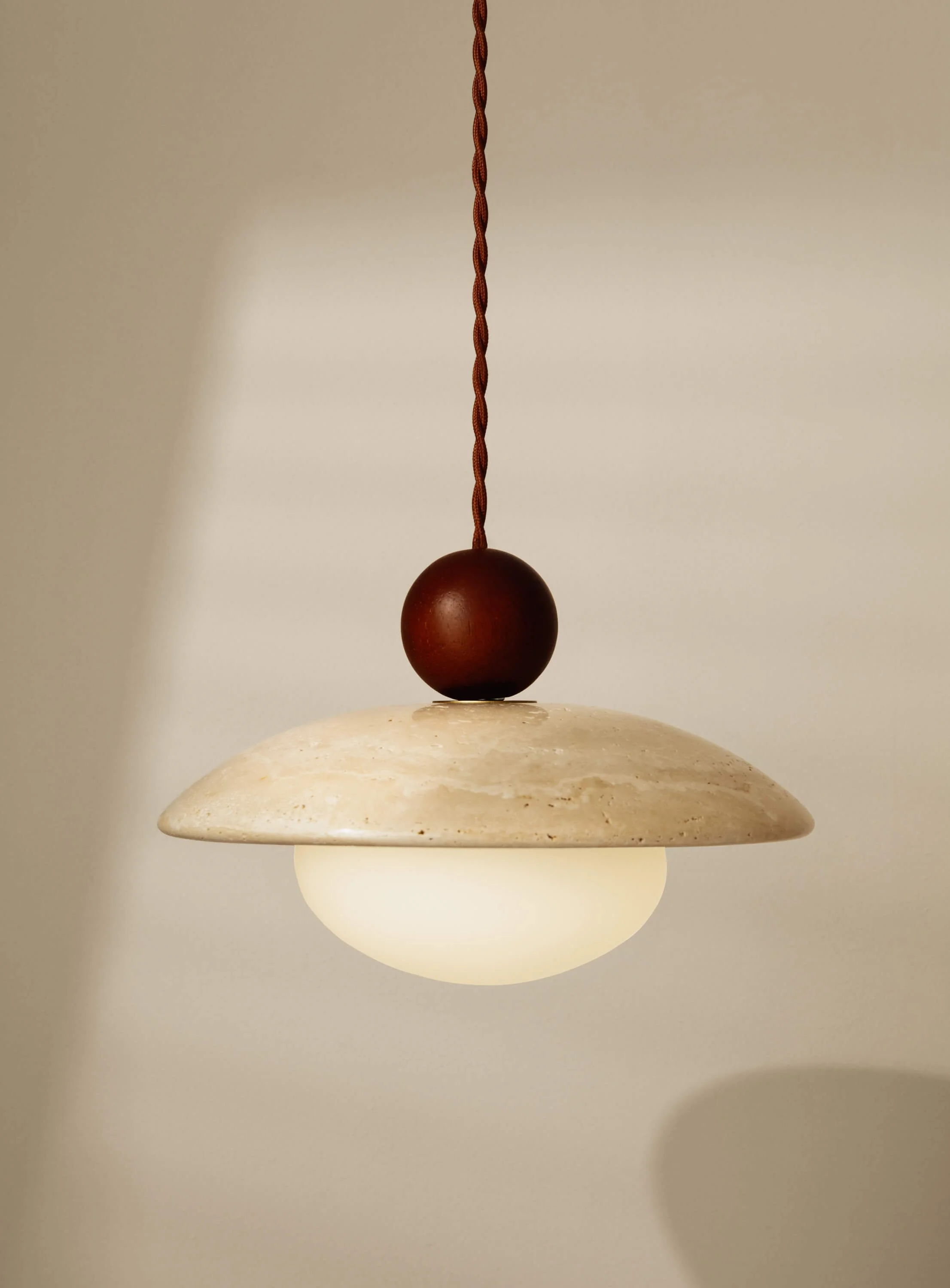 A modern pendant light fixture with a round cream-colored stone or marble shade, a frosted glass diffuser, and a dark brown decorative element on top, hanging from a brown twisted cord.