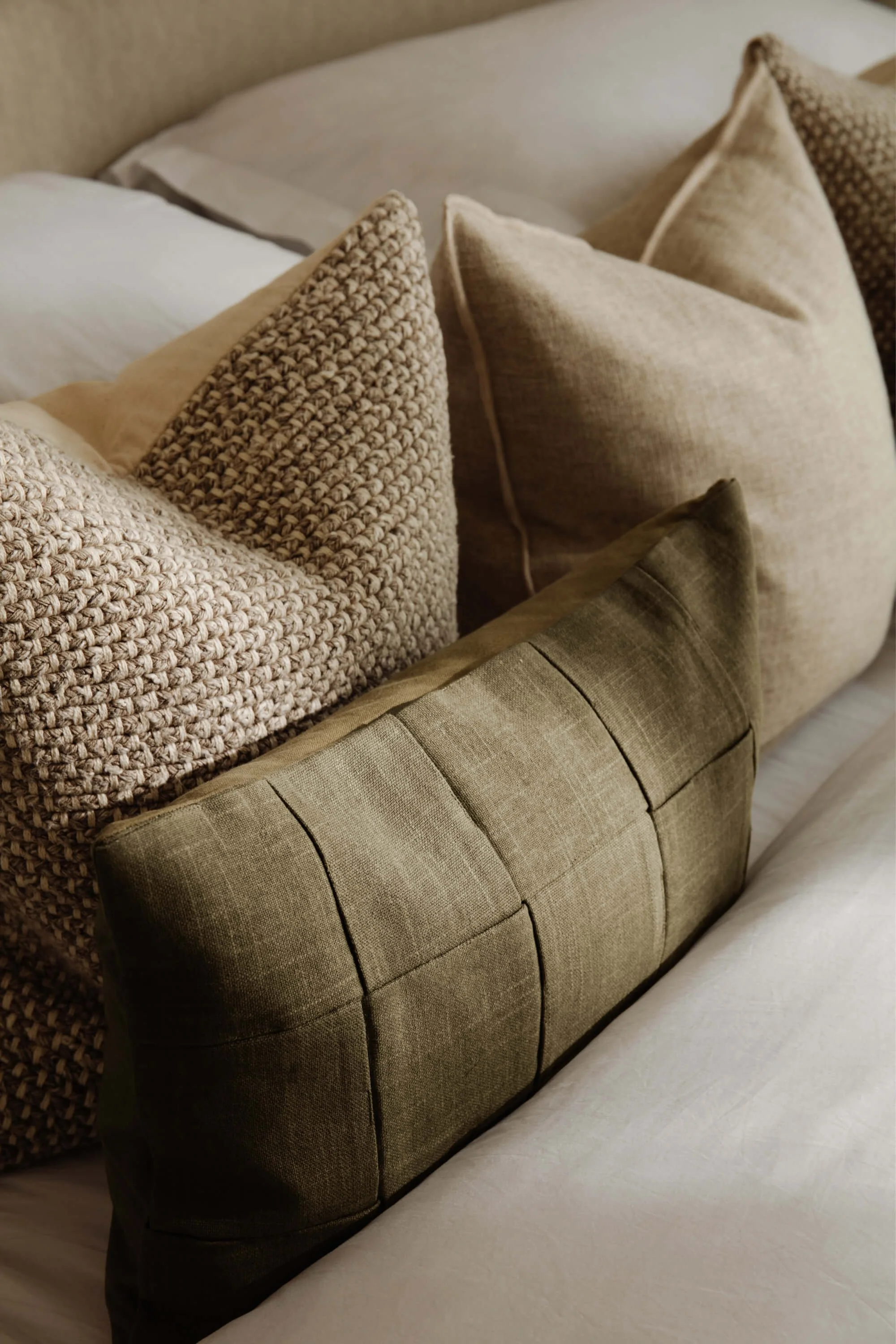 A collection of various beige and olive green throw pillows on a bed.