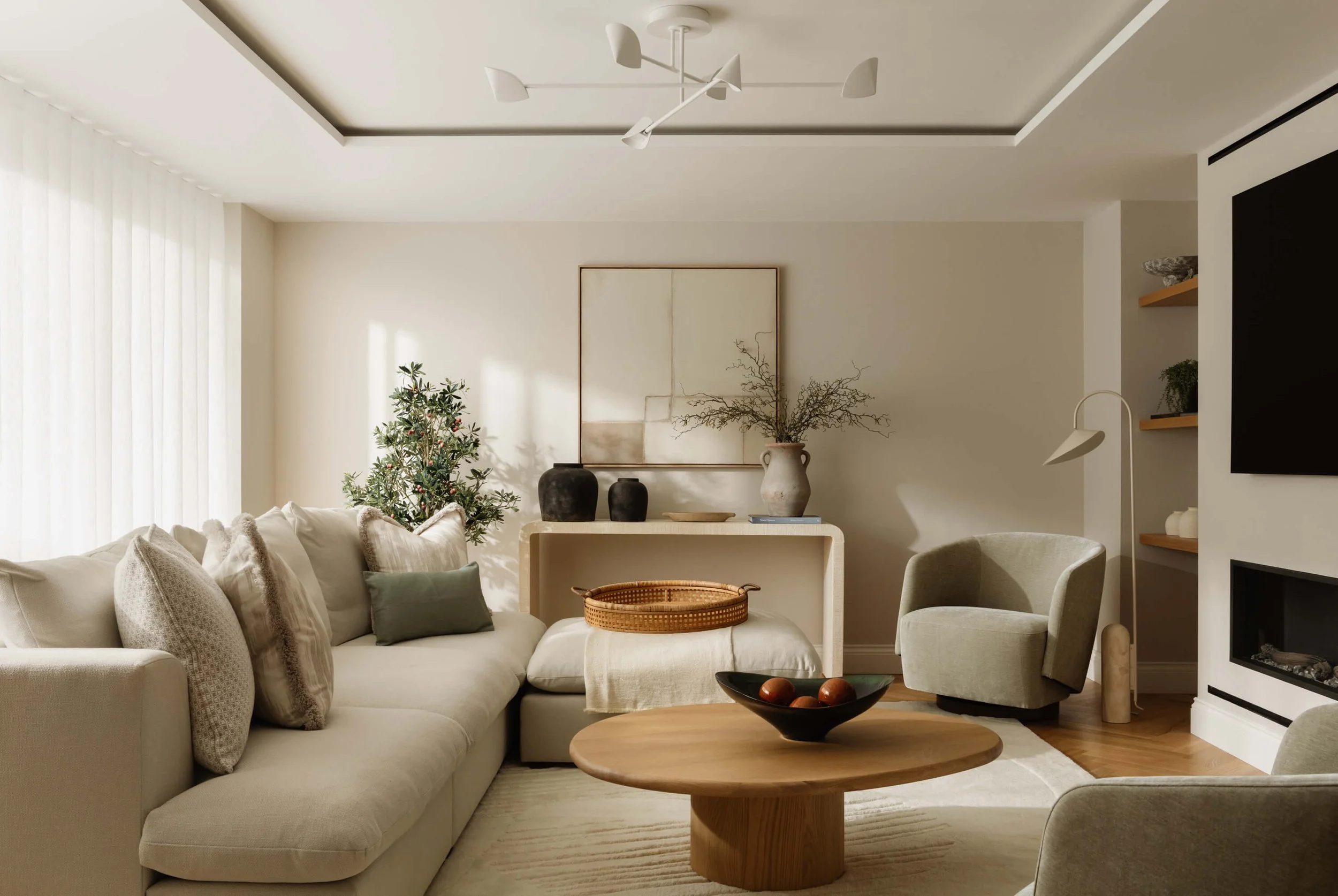 Modern living room with cream sofa, armchair, wooden coffee table, decorative pillows, Christmas tree, wall art, and minimalist decor.