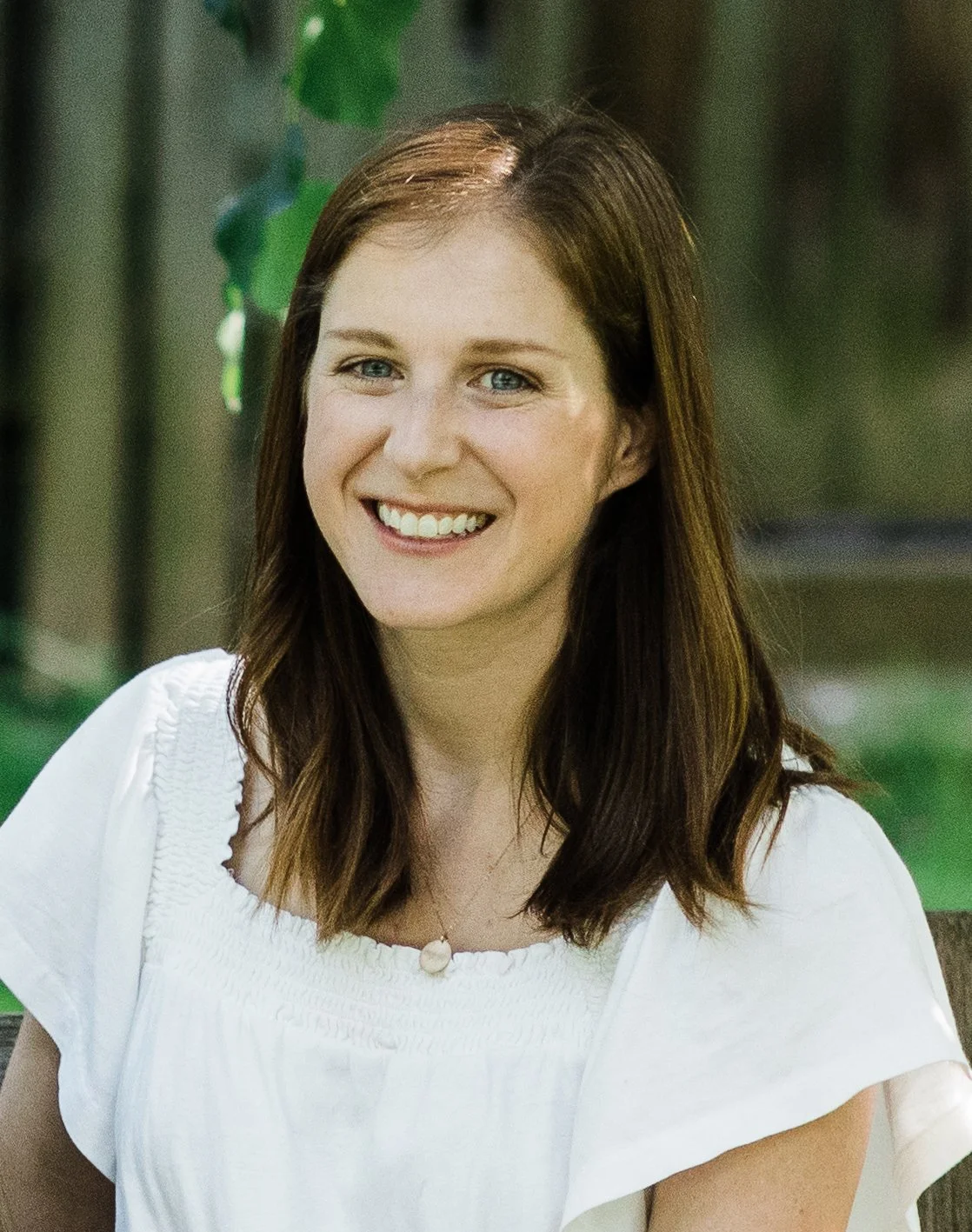 Portrait of a Kelly Mairs outdoors with green foliage in the background.