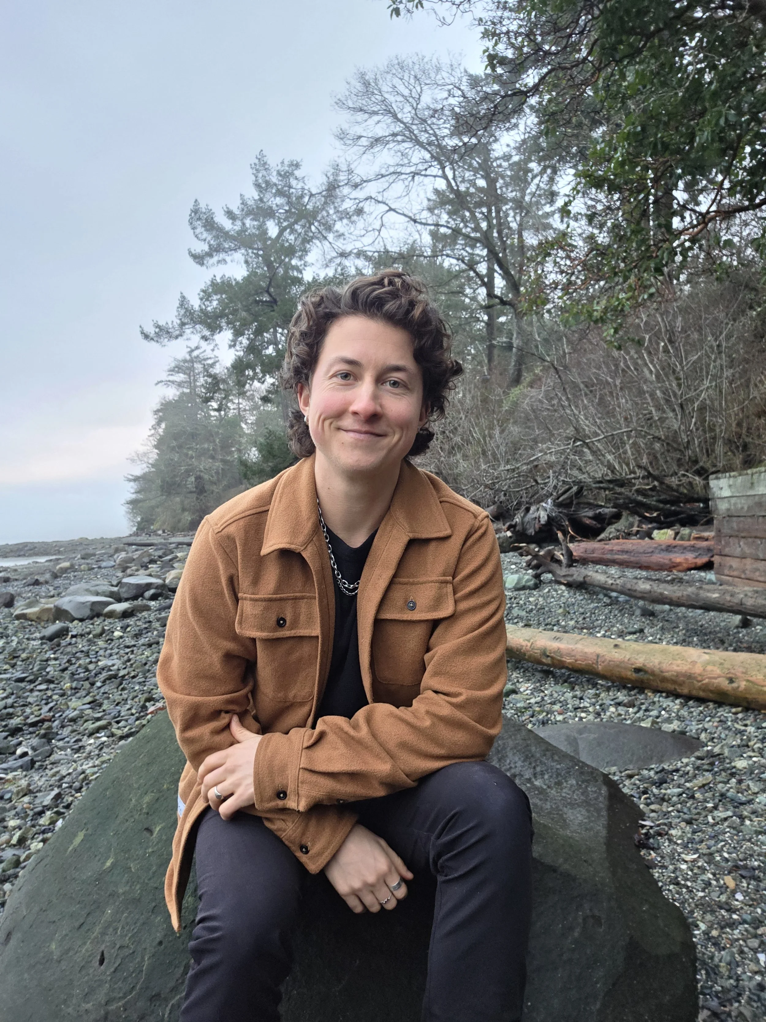 A person standing on a wooden bridge surrounded by trees in a forest, holding onto the railing and looking up with a smile.