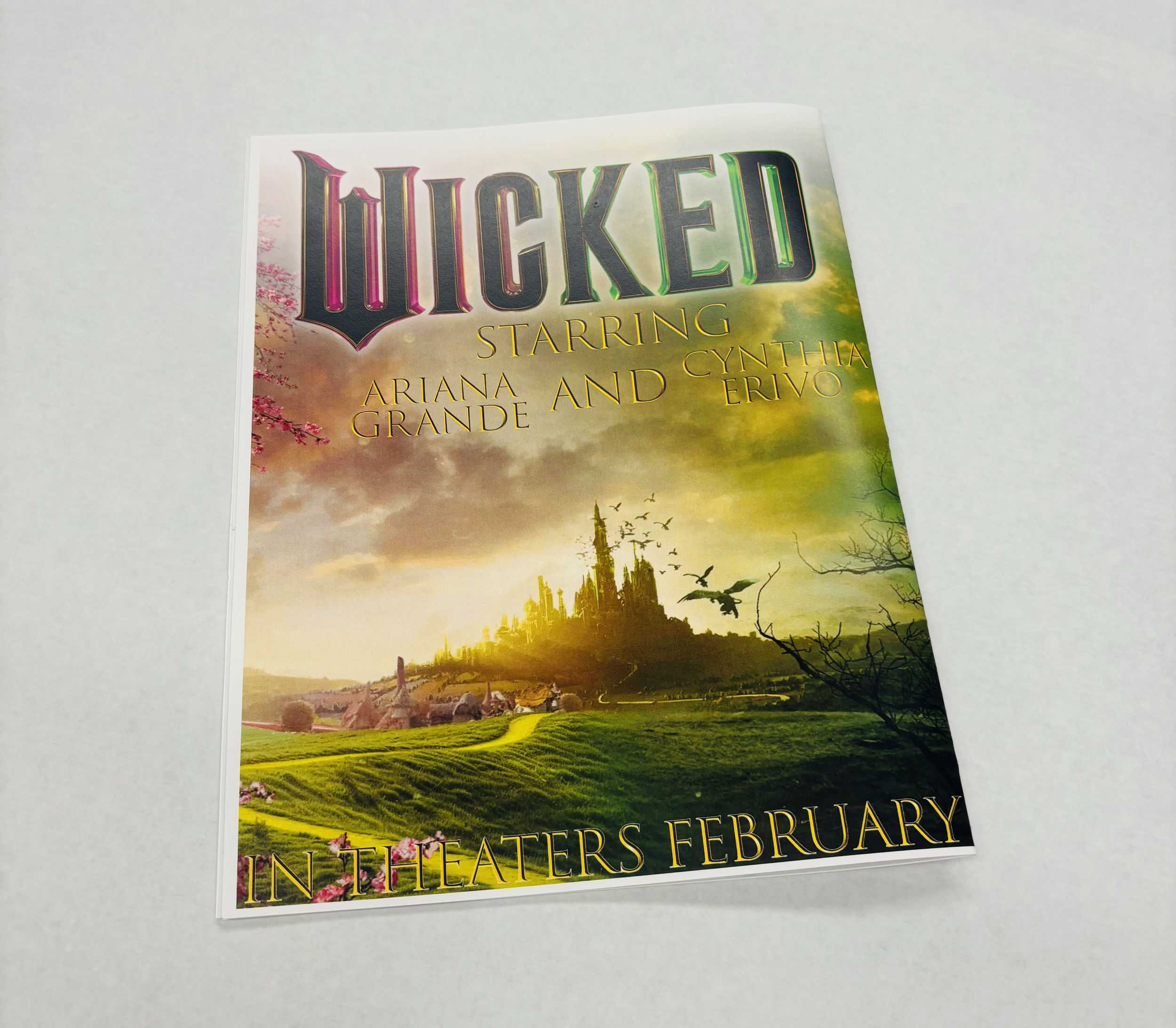 Promotional flyer for the musical Wicked featuring Ariana Grande and Cynthia Erivo, showing a fantasy landscape with a castle, birds, and a cloudy sky, indicating a February theater release.