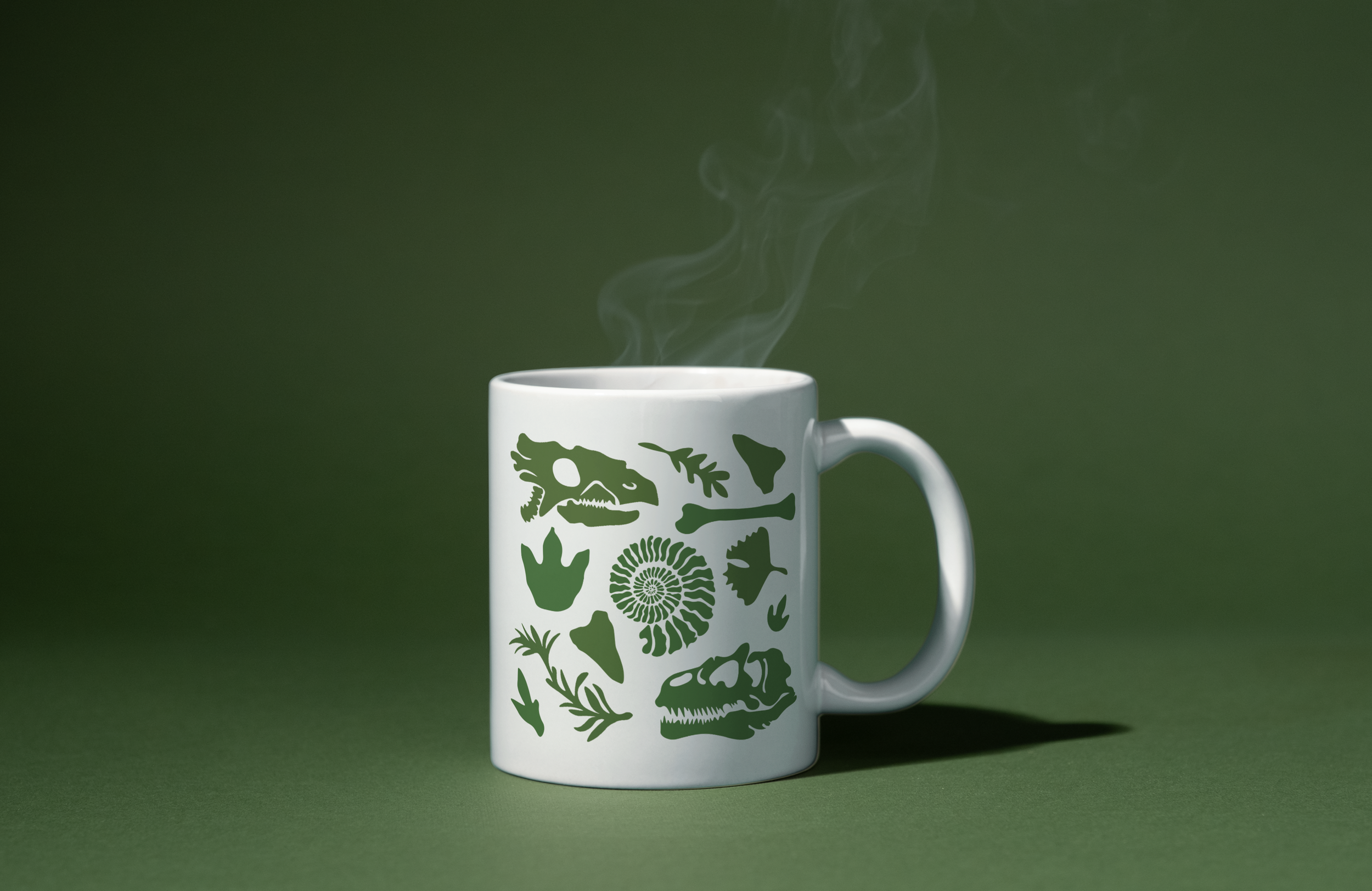 White coffee mug with green dinosaur and fossil designs, steaming against a dark green background.