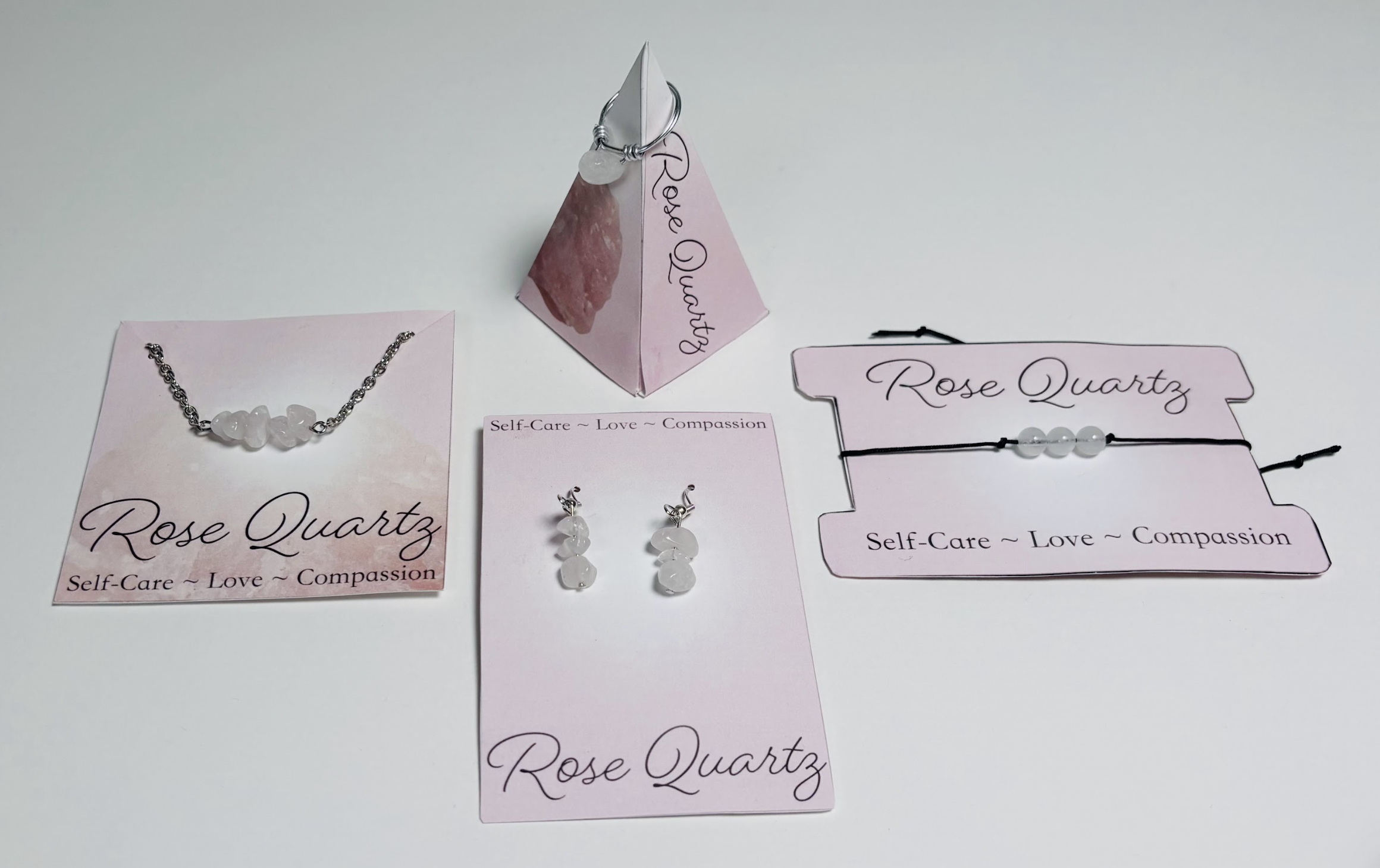 Jewelry display with rose quartz jewelry pieces and pink cards labeled 'Rose Quartz' with the words 'Self-Care ~ Love ~ Compassion'.