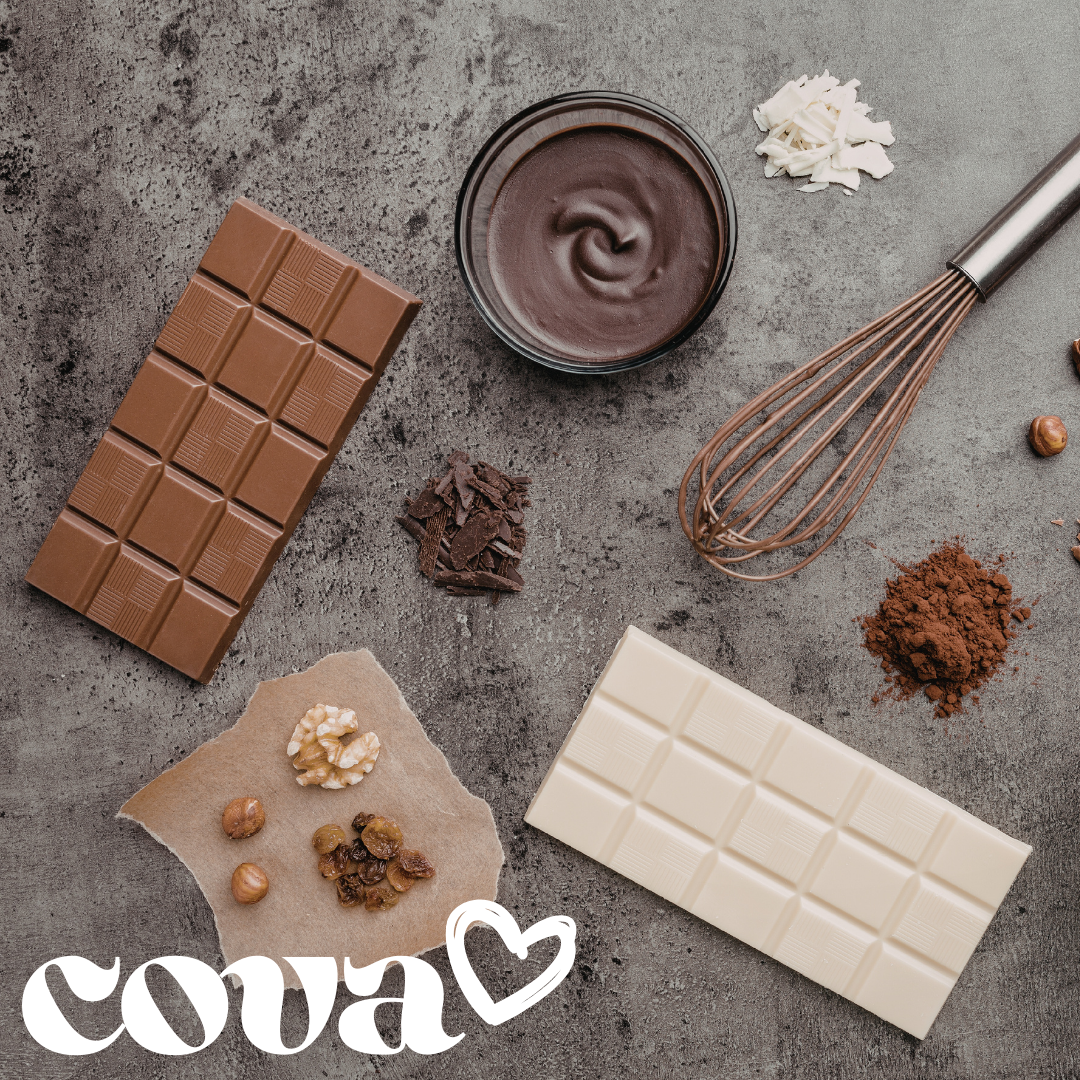 Assorted ingredients for making chocolate, including milk and white chocolate bars, a bowl of melted chocolate, chopped white chocolate, chocolate shavings, cocoa powder, chopped nuts and raisins, and a whisk on a gray surface. "COVA" with a heart sy