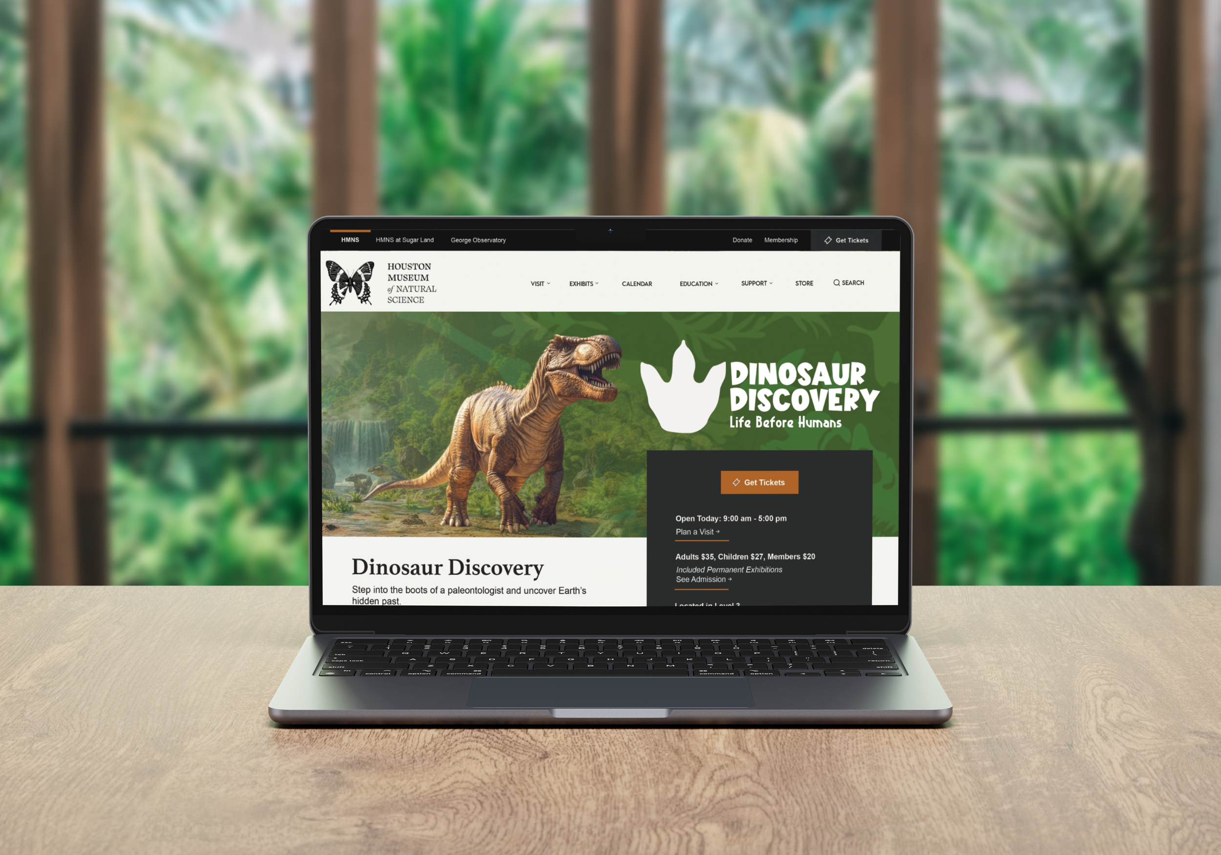 Laptop displaying the Houston Museum of Natural Science's Dinosaur Discovery exhibit webpage, with a dinosaur image and green background, set on a wooden table with a blurred green tropical background.