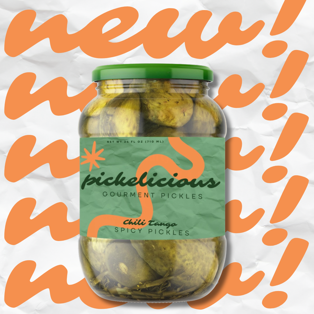 A jar of Pickledicious Gourmet Pickles with spicy chili flavor, featuring a green lid, inside the jar are pickles submerged in brine, placed on crumpled white paper with orange stylized text in the background.