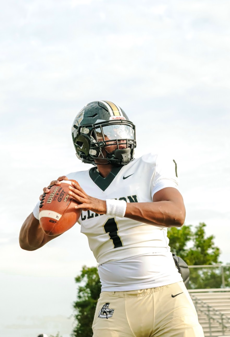 A football player wearing a helmet and a white jersey with the number 1, holding a football ready to throw, standing outdoors on a cloudy day.