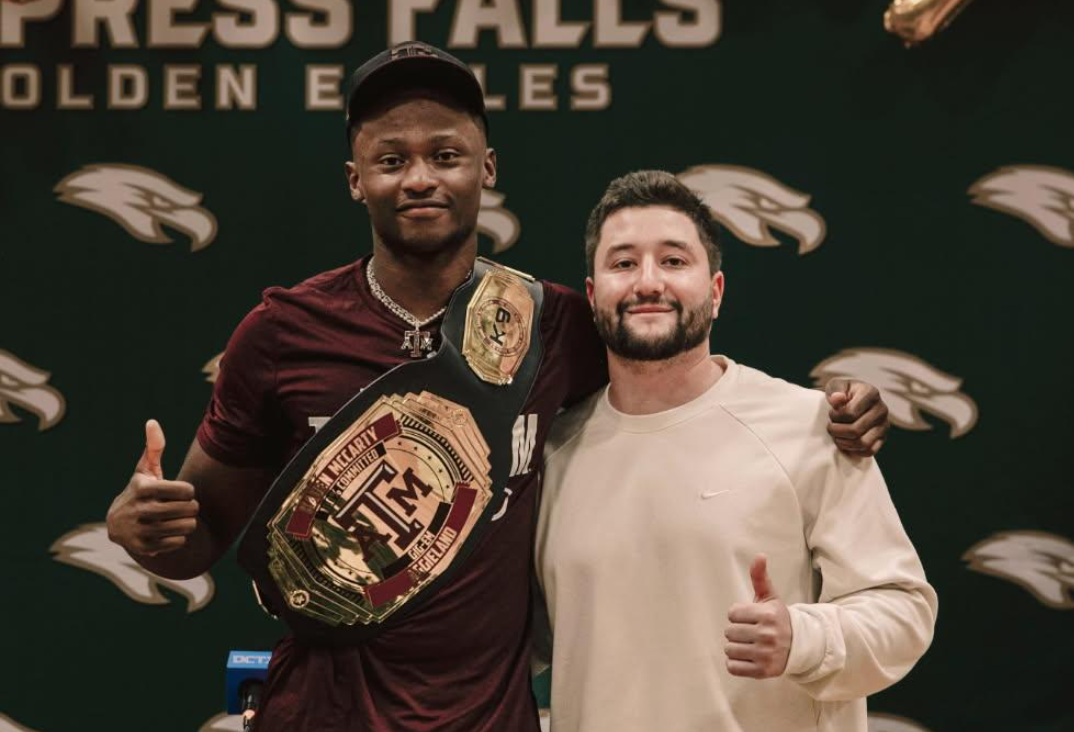 A football player with a championship belt around his shoulder, standing next to a man giving a thumbs up, in front of a backdrop with Eagles logos and the words "Press Fails".