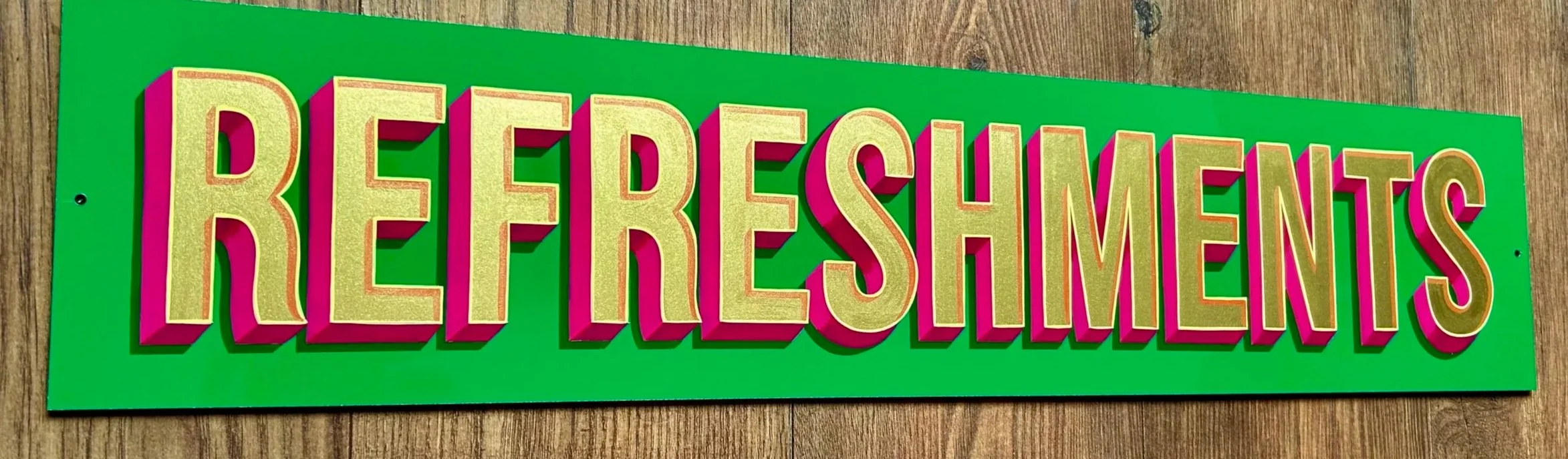 Colorful sign that reads 'REFRESHMENTS' in large gold letters with pink shadows on a green background, placed on a wooden surface.