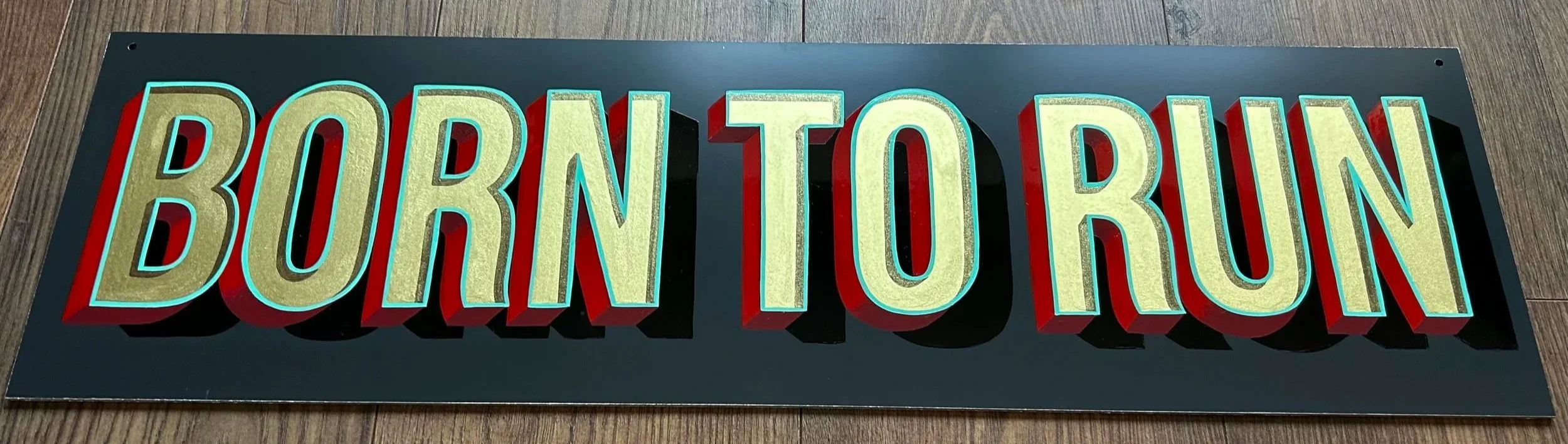 A decorative sign with large block letters spelling 'BORN TO BUY' on a dark background, placed on a wooden floor.