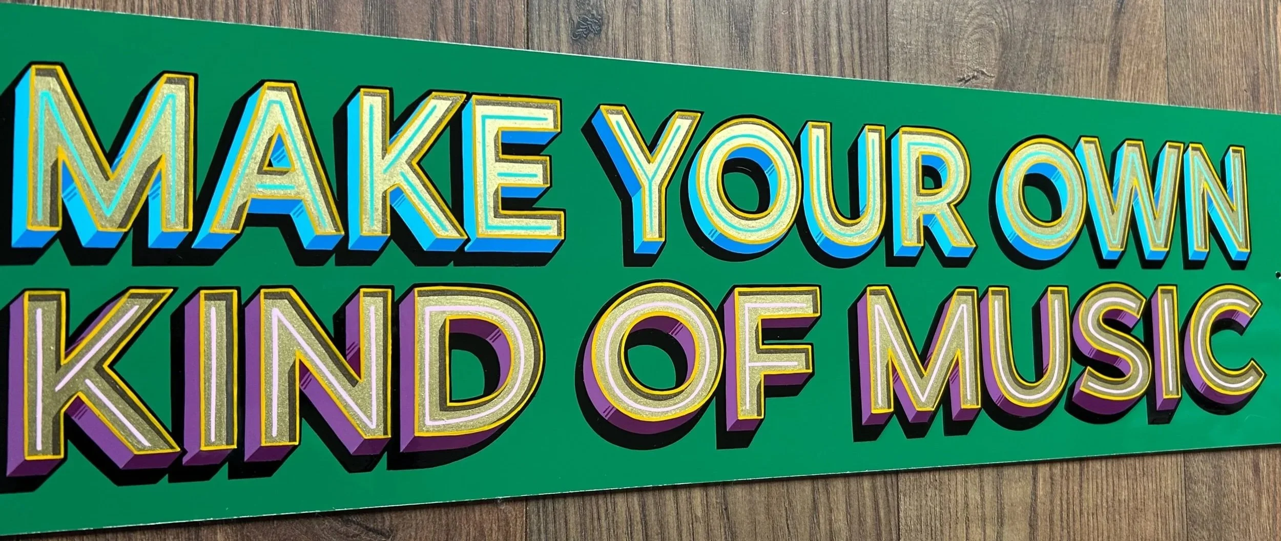 Colorful sign with the text 'Make Your Own Kind of Music' on a green background, placed on a wooden floor.