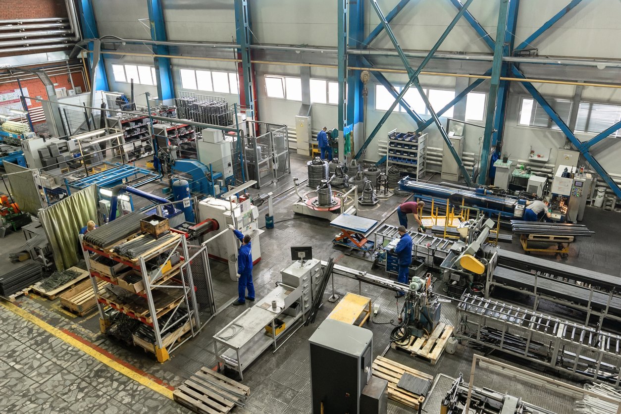 An industrial factory with workers operating machinery, metal parts, and equipment for manufacturing or assembly in a factory setting.