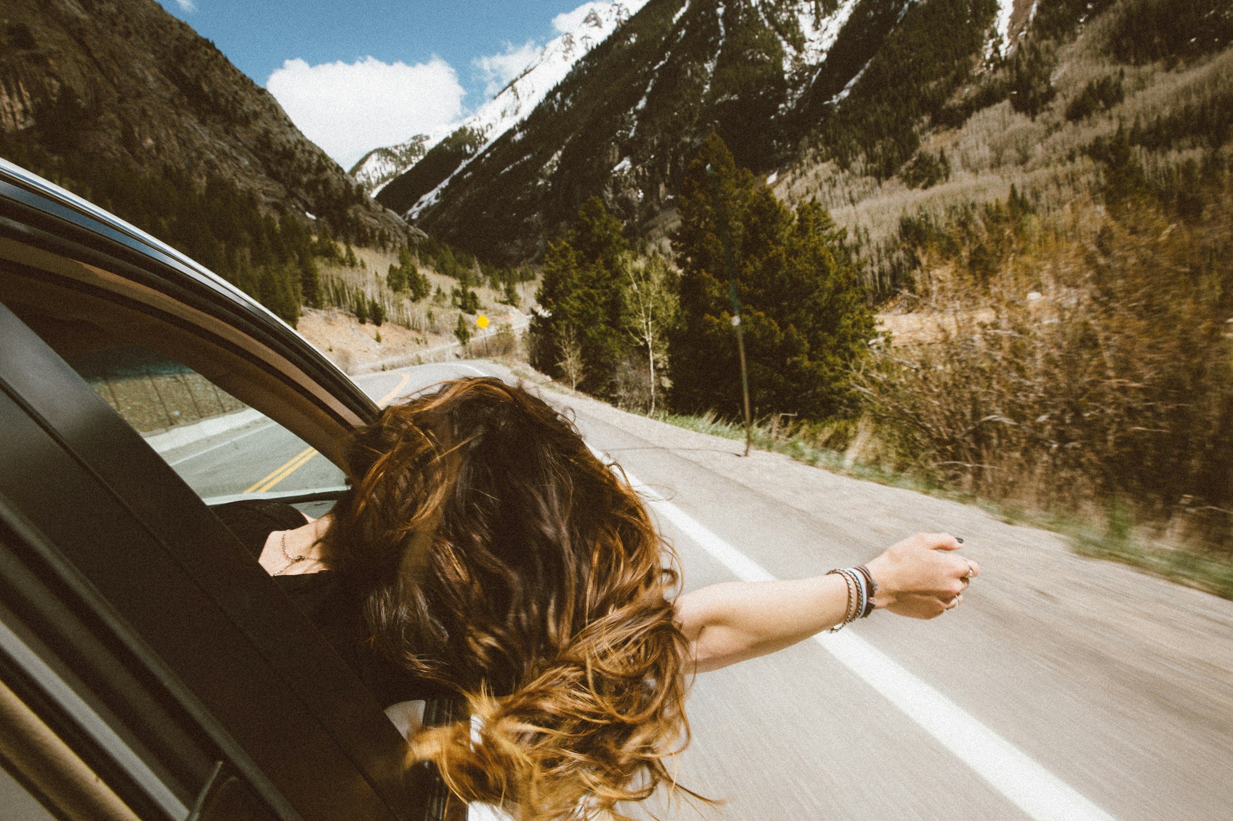 Woman leaning out of a car on a winding mountain road, symbolizing midlife mental reset and clarity through guided hypnosis.