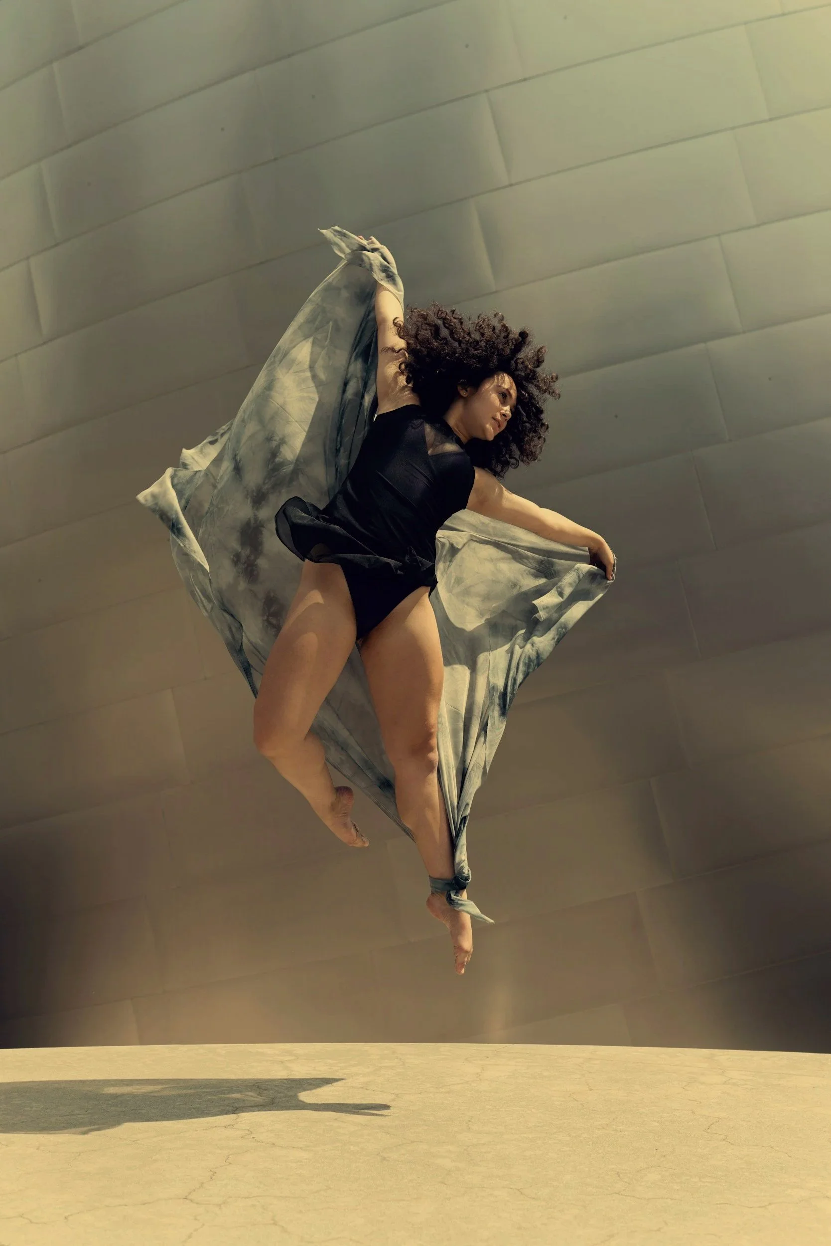 Woman performing an expressive leap with flowing fabric indoors, representing freedom, emotional release, and personal transformation.