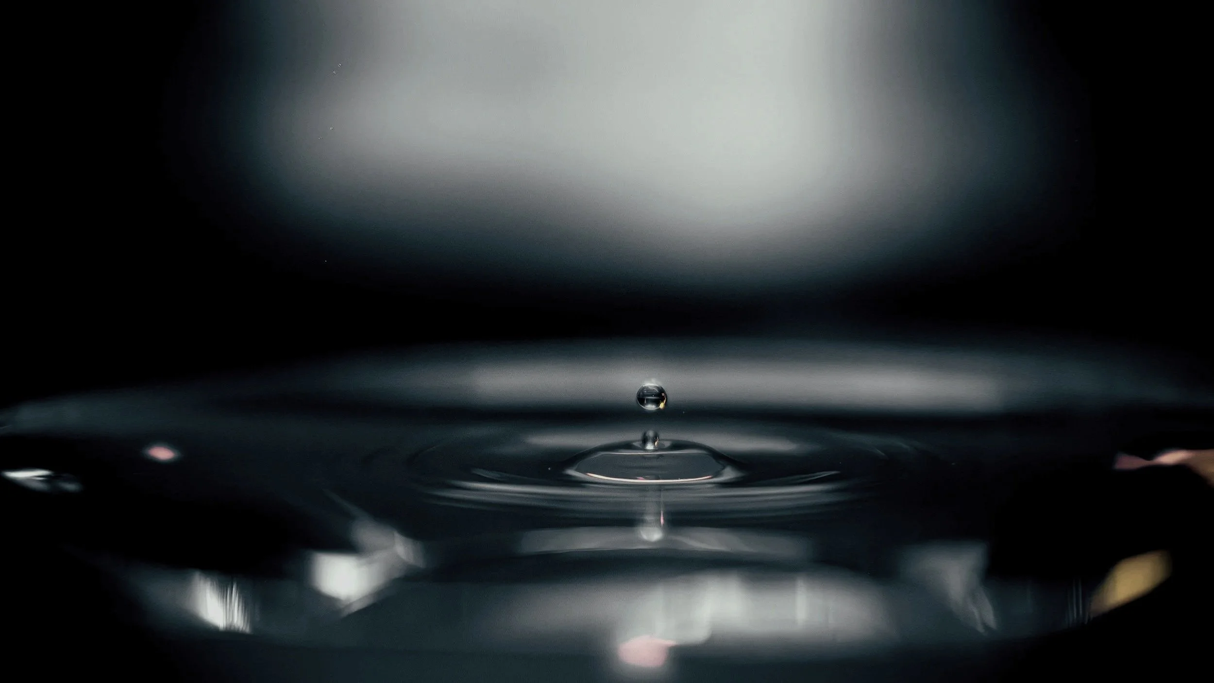 A macro photograph of a single water droplet hitting a dark surface, creating calm ripples to symbolize nervous system regulation.