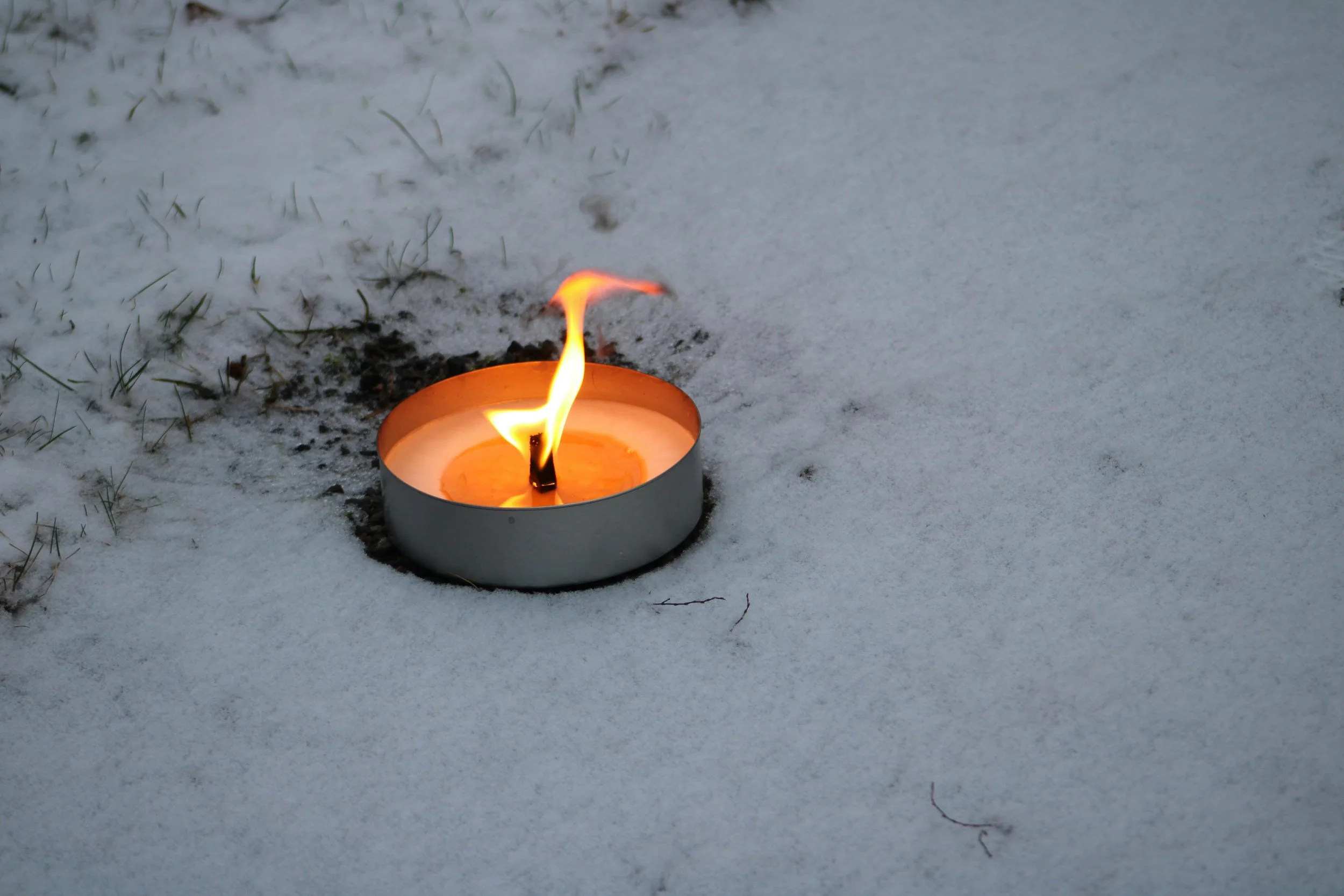A single candle burning steadily in the snow, representing intentional warmth and inner steadiness during the Snow Moon.
