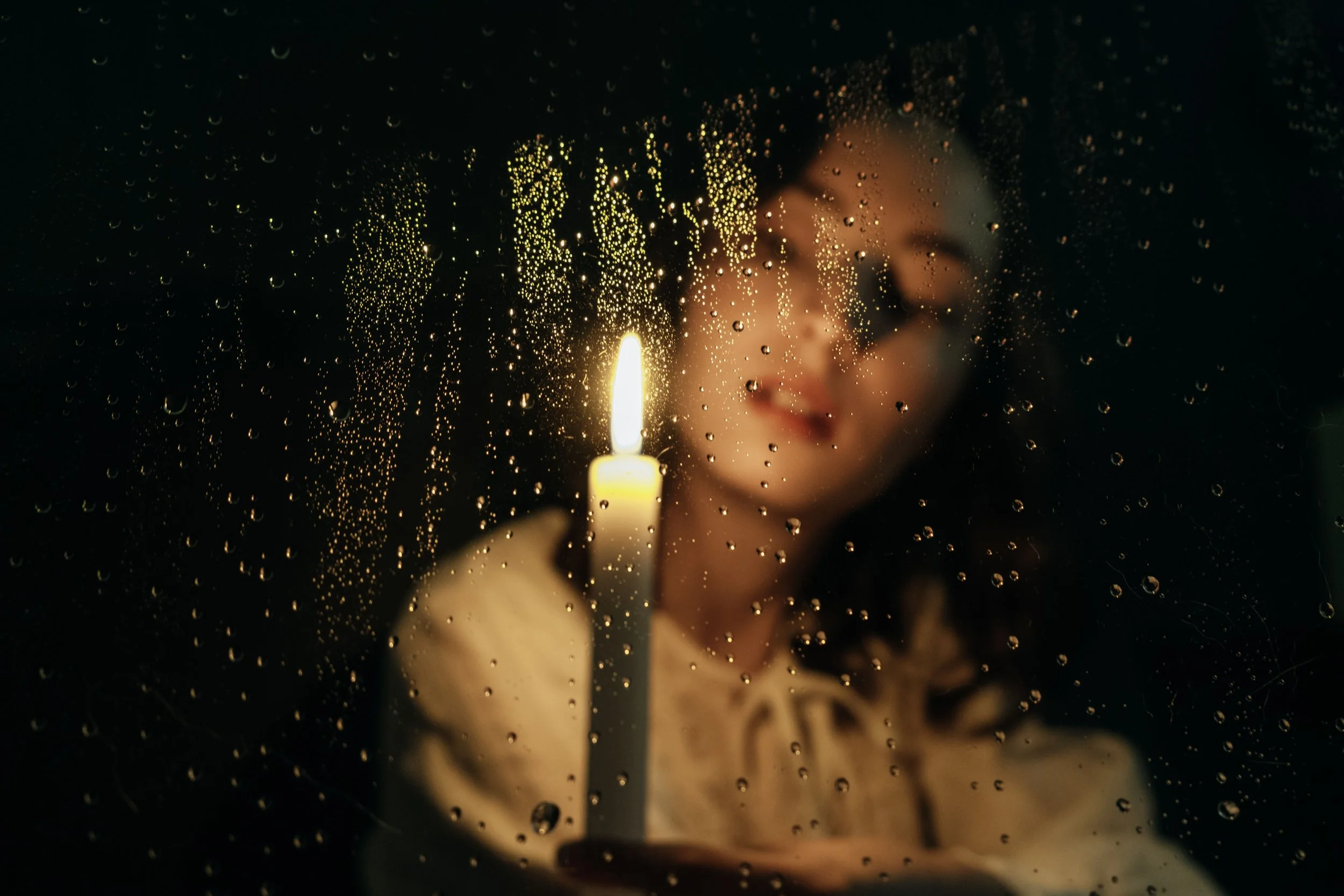 Woman holding a lit candle behind a rain-streaked window, header image for the blog post What Is DBT and Why I Bring It Into Every Bodywork Session.