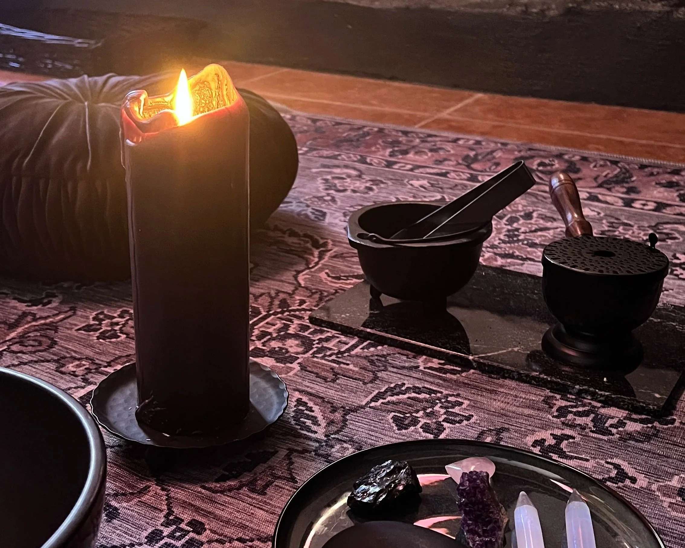 Black candle burning on a dark altar with mortar and pestle, crystals, and incense holder on a patterned rug, evoking nervous system healing ritual at Veluna Wellness.