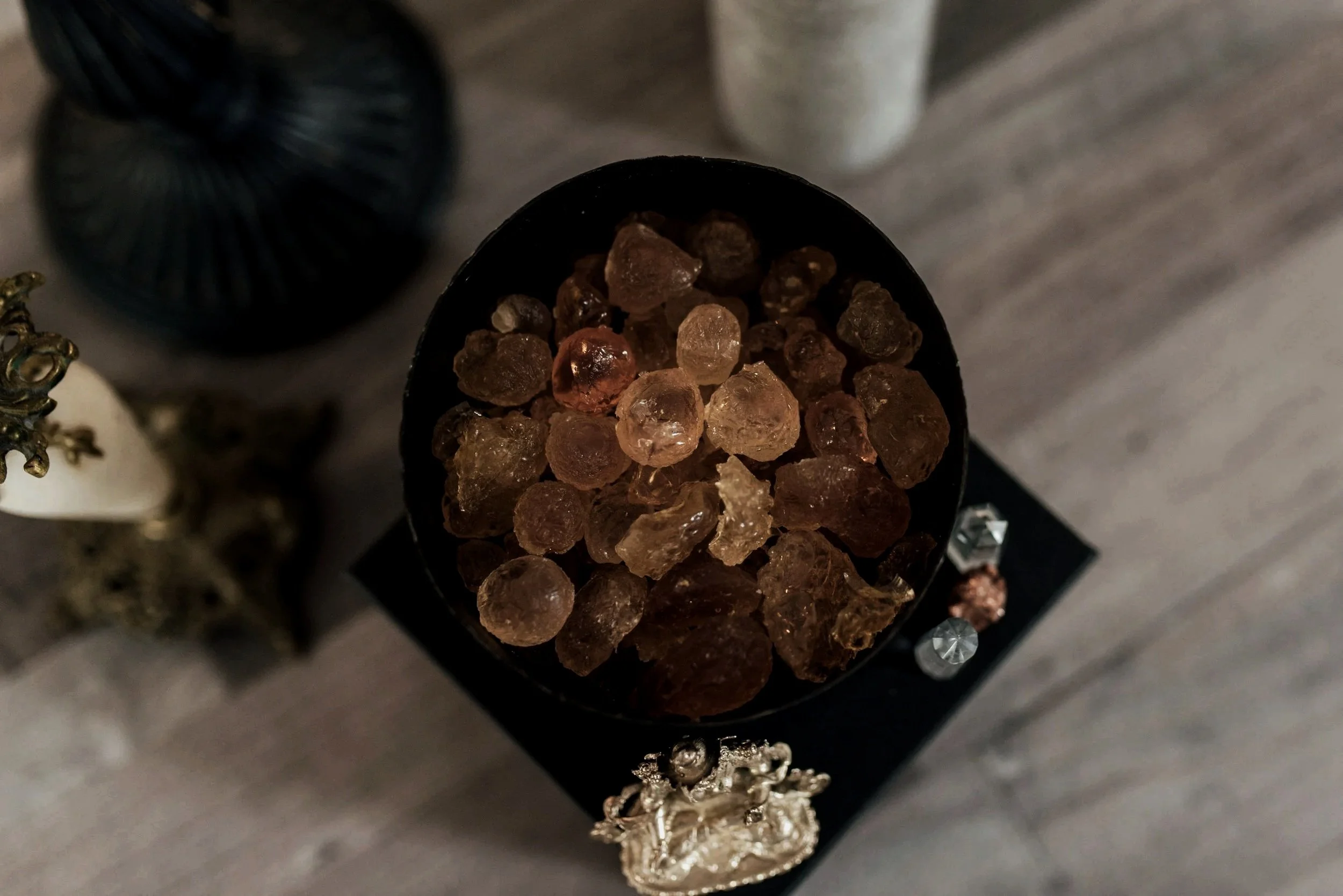 Overhead view of frankincense resin in a dark bowl surrounded by ritual objects, representing somatic healing and nervous system regulation