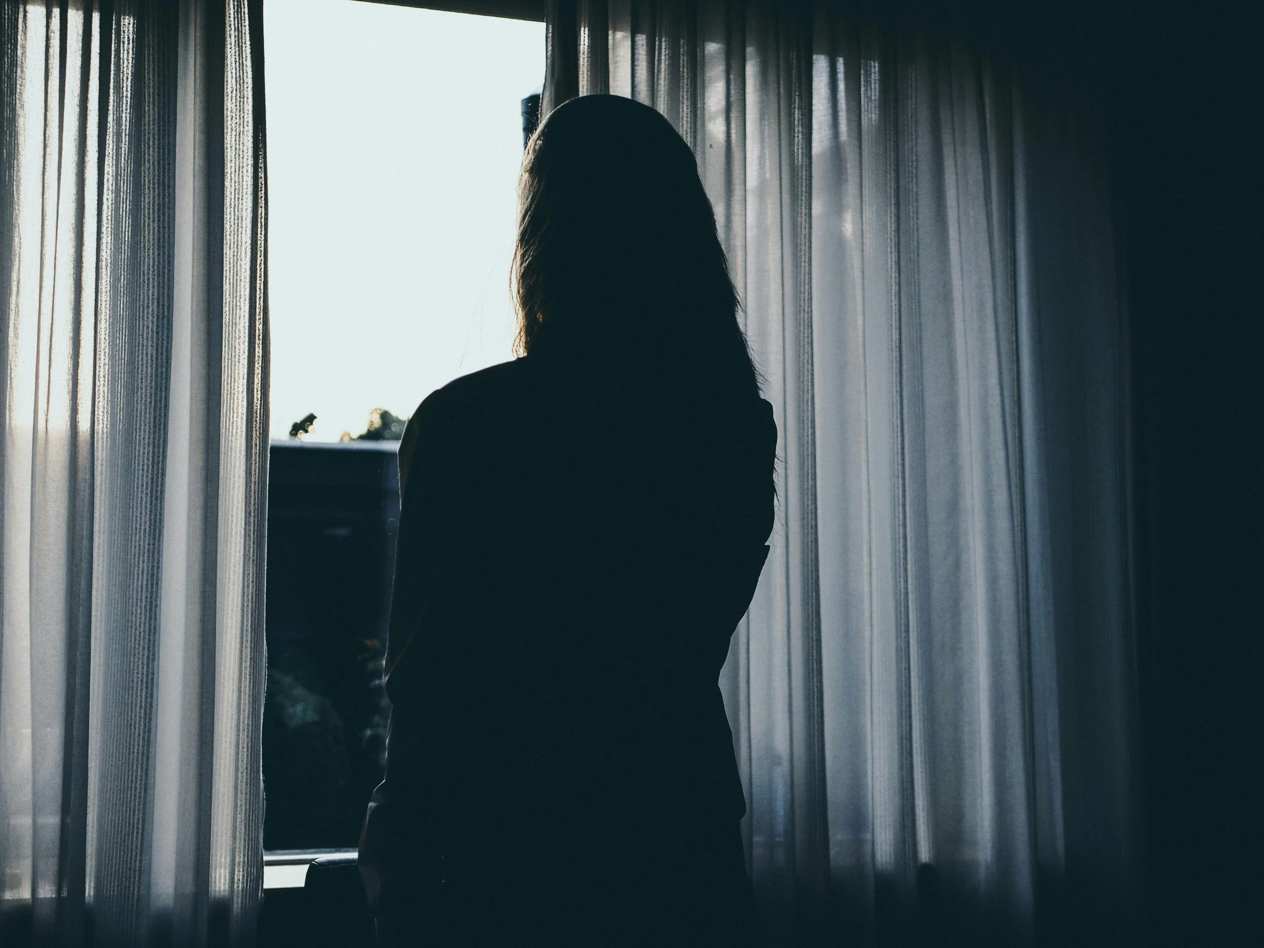 Silhouette of a woman standing at a window, representing somatic grief and the body holding loss