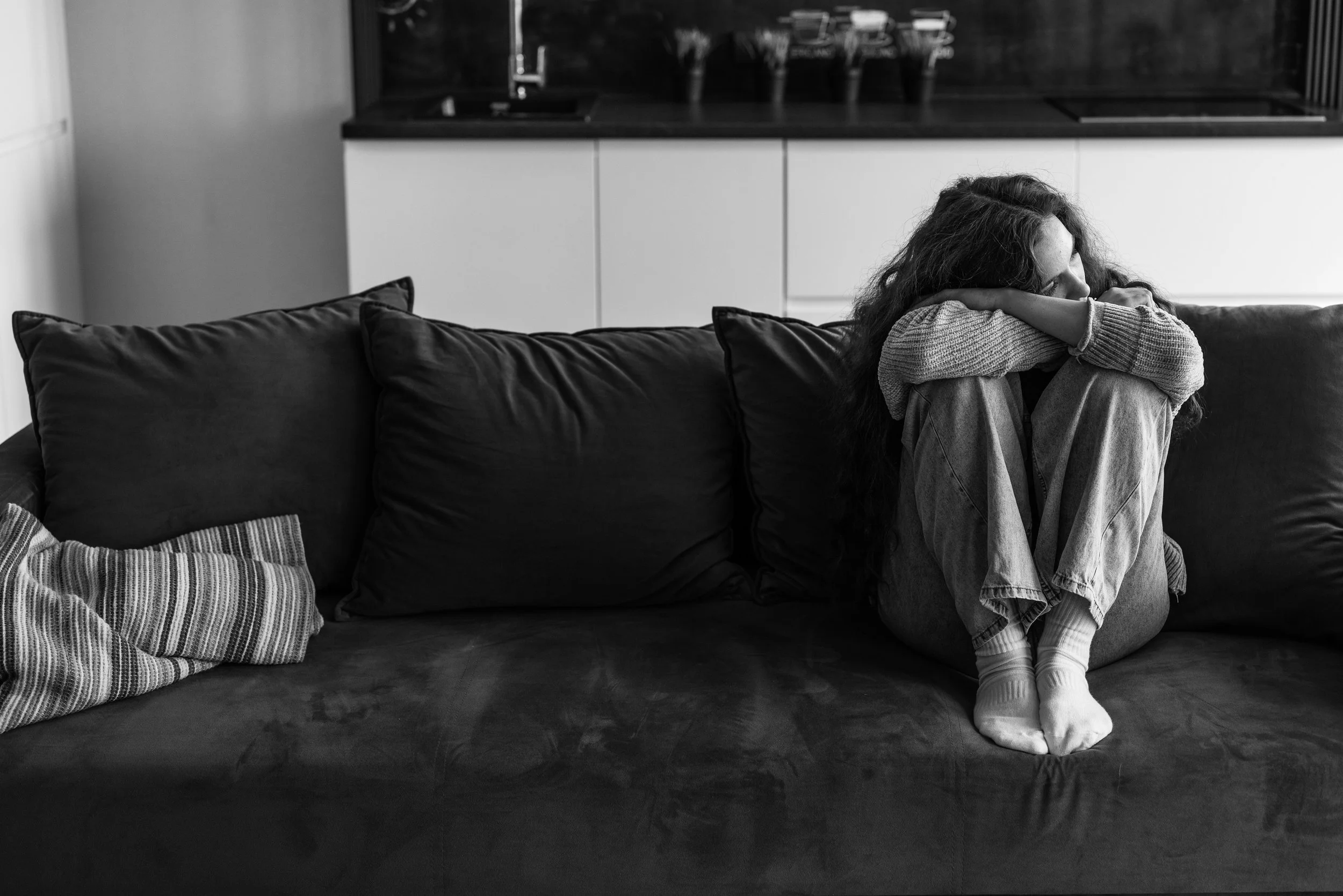 Woman sitting curled up on a couch with her head down, illustrating that healing does not mean feeling calm all the time.