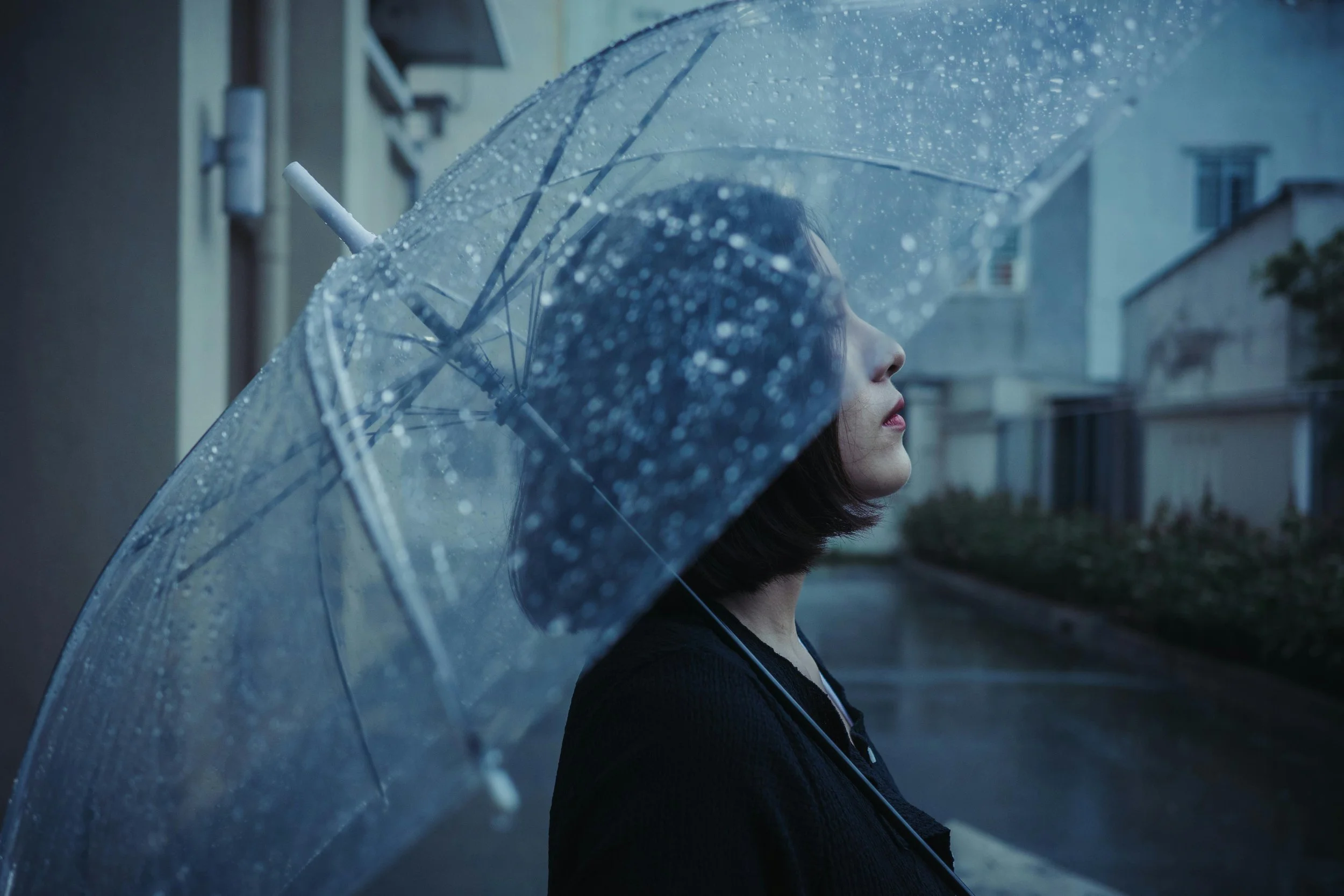 A person standing outdoors under a clear umbrella in the rain.