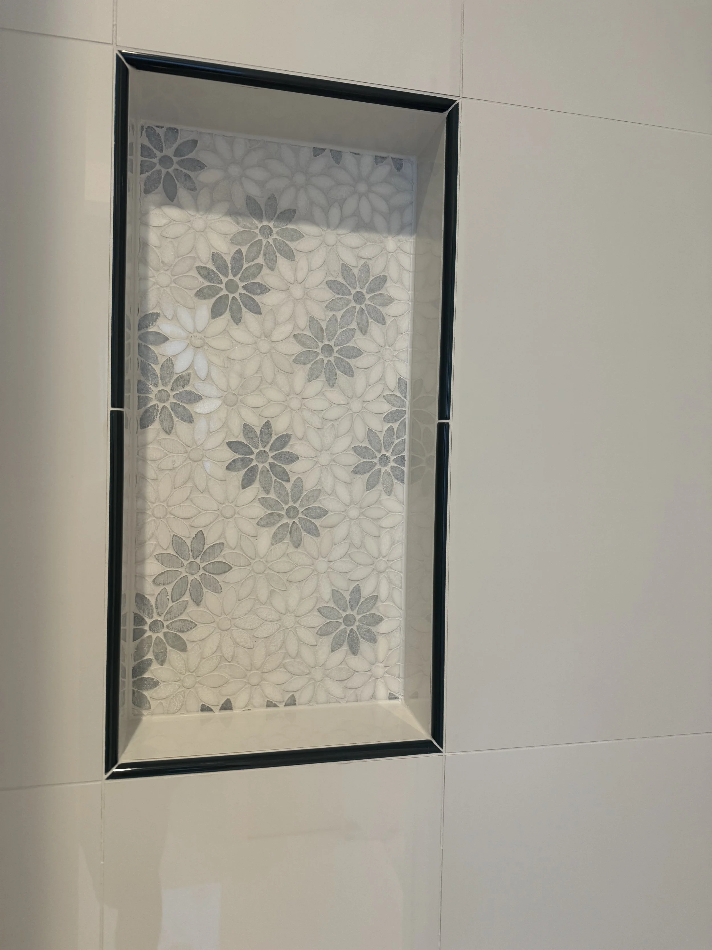 Decorative wall niche with floral-patterned tile background, surrounded by beige wall tiles.