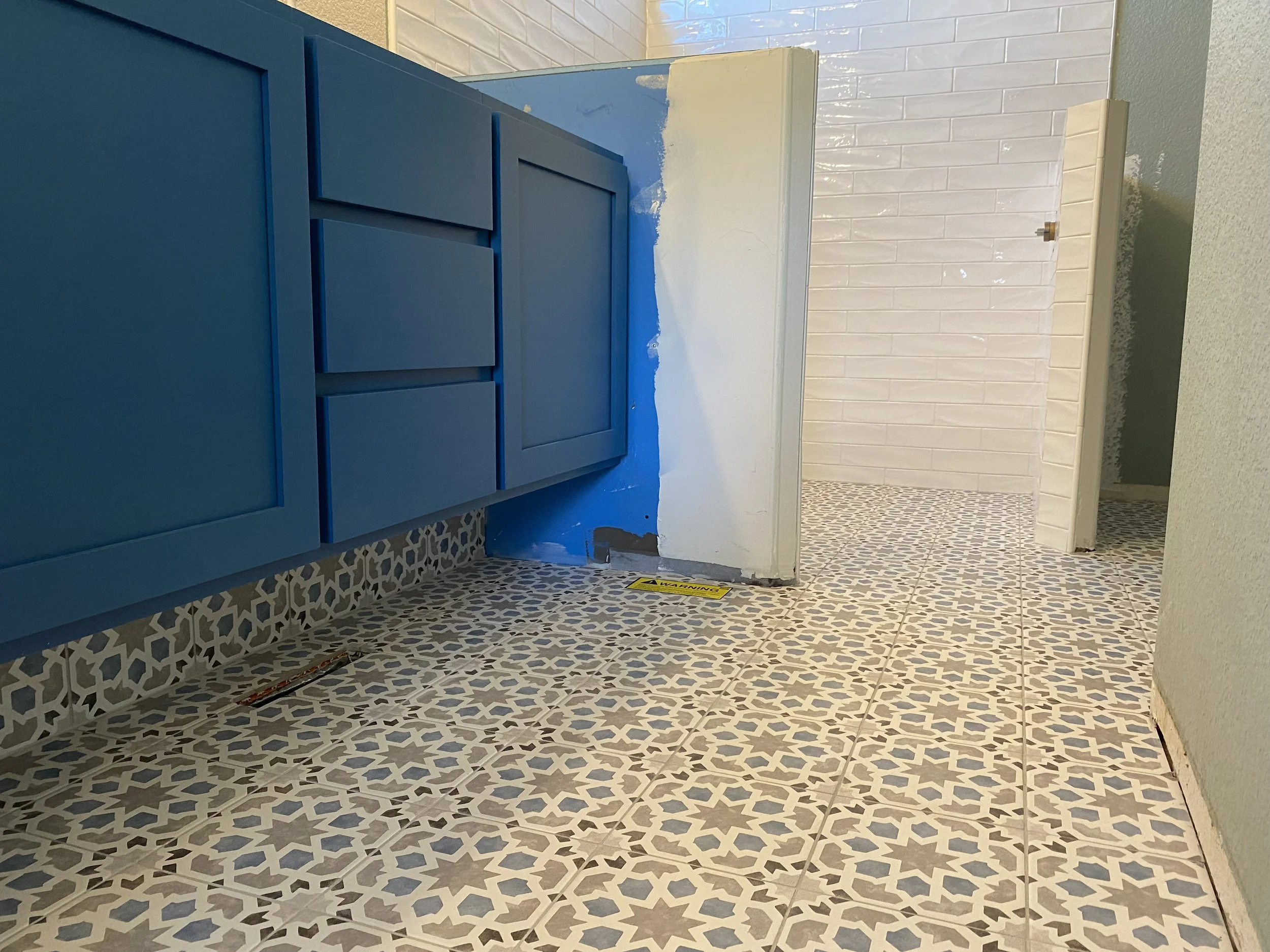 Bathroom with blue cabinetry, patterned tile floor, partially painted wall, and open shower with white subway tile walls.
