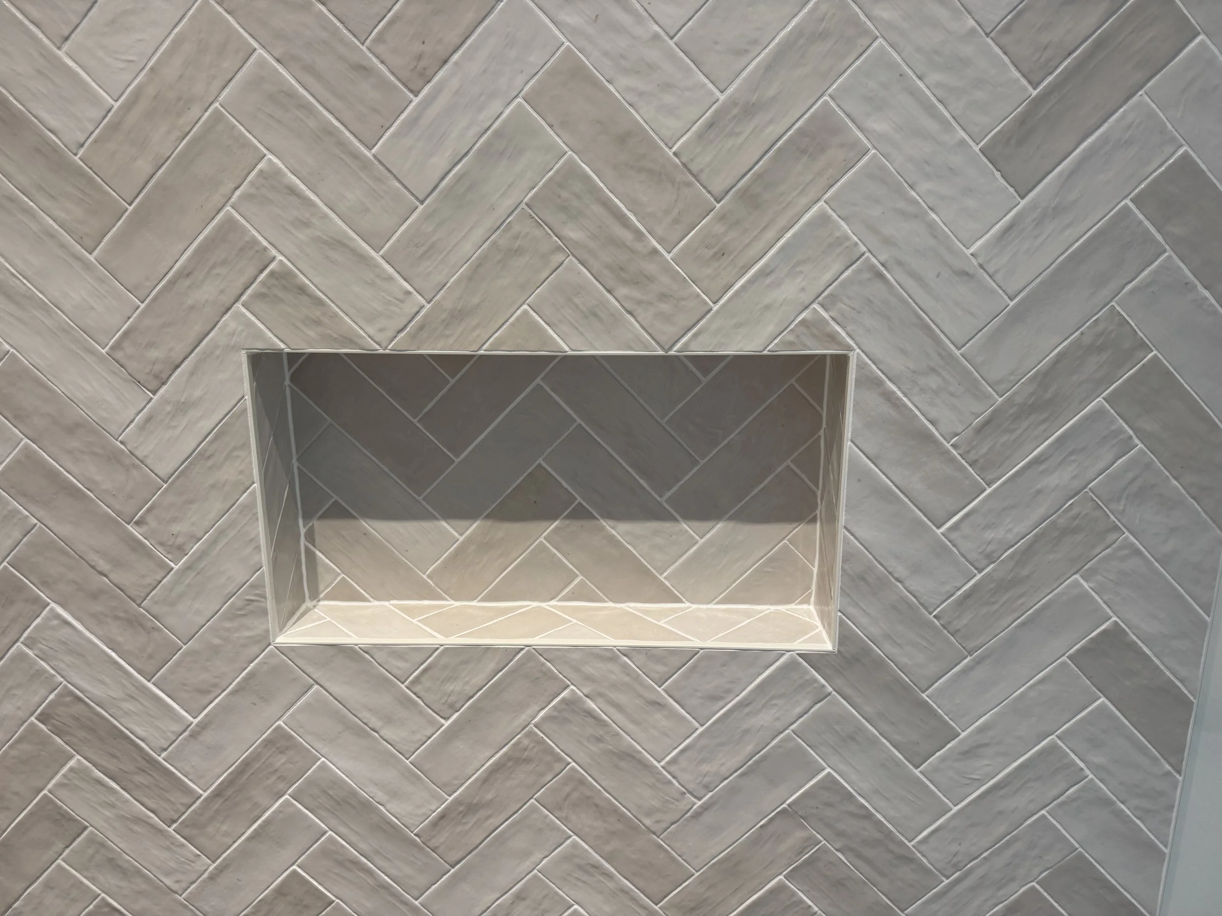 A recessed shelf built into a herringbone-pattern tiled wall.