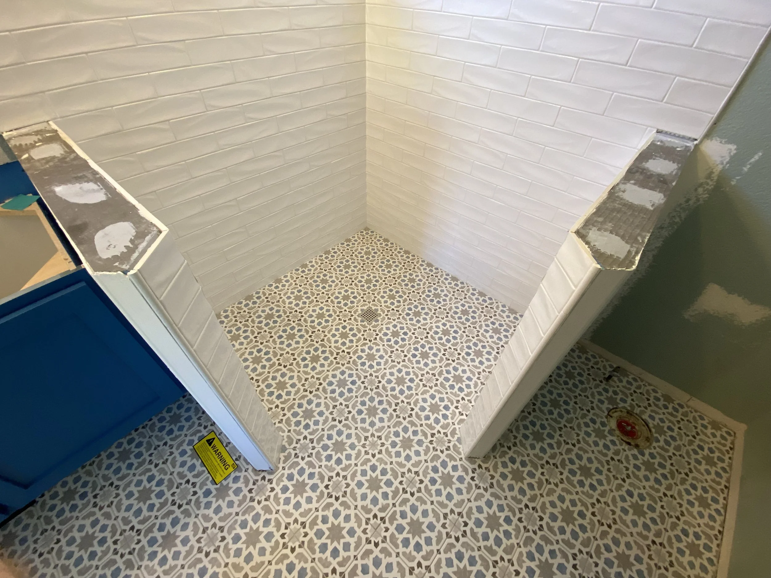 Tile bathroom floor with a drain and white tile walls, surrounded by partially installed cabinetry and walls.