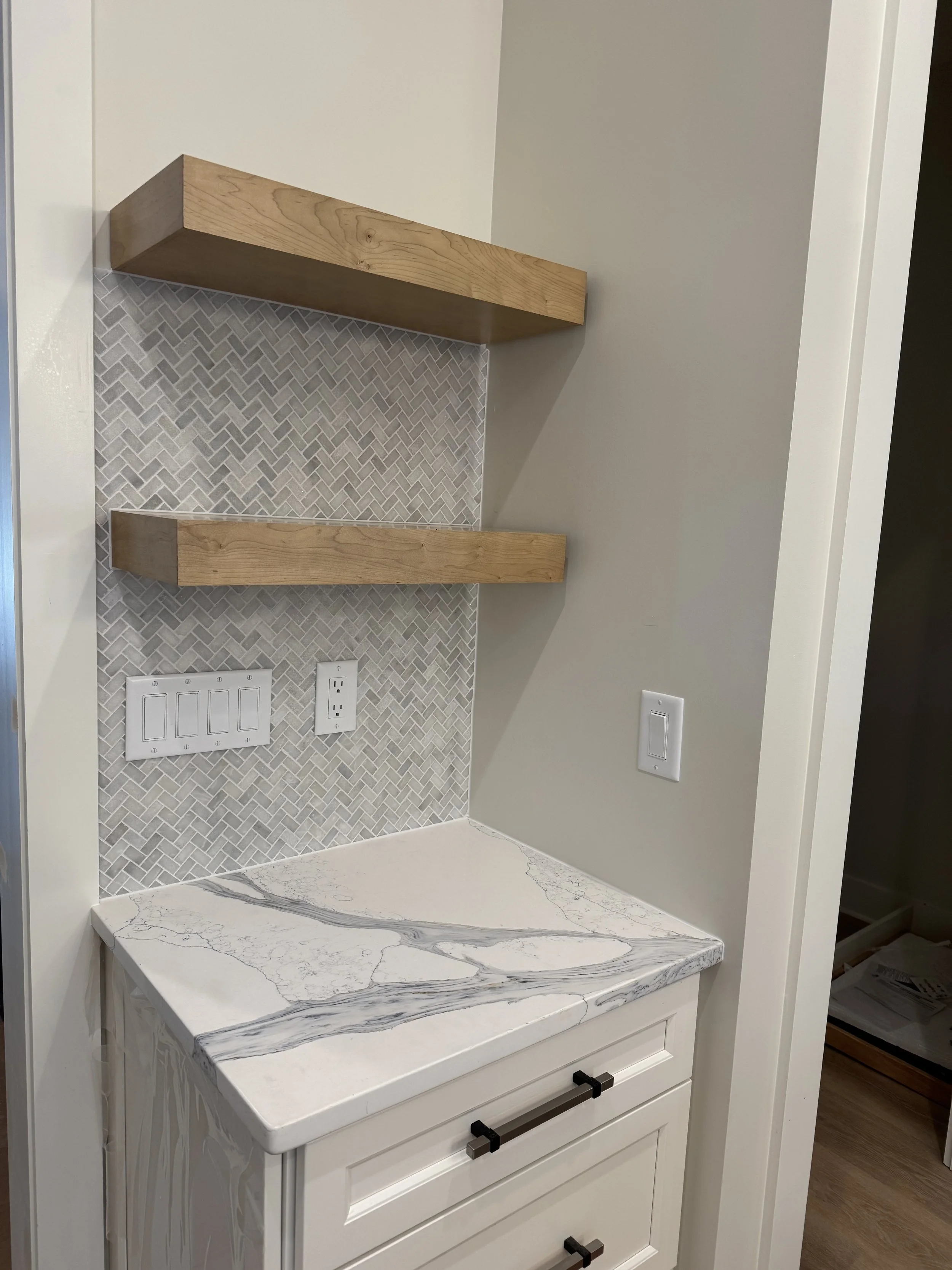 A section of a kitchen or workspace with a marble countertop, two wooden shelves, and wall outlets.