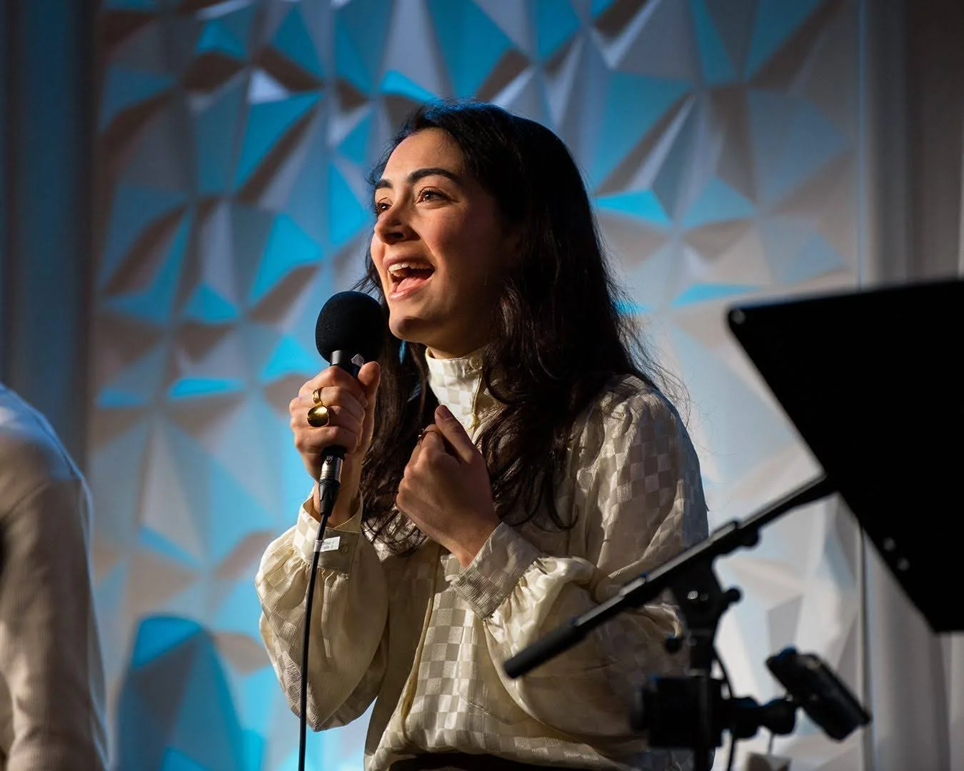 Woman singing into a microphone at an indoor event with geometric wall design.