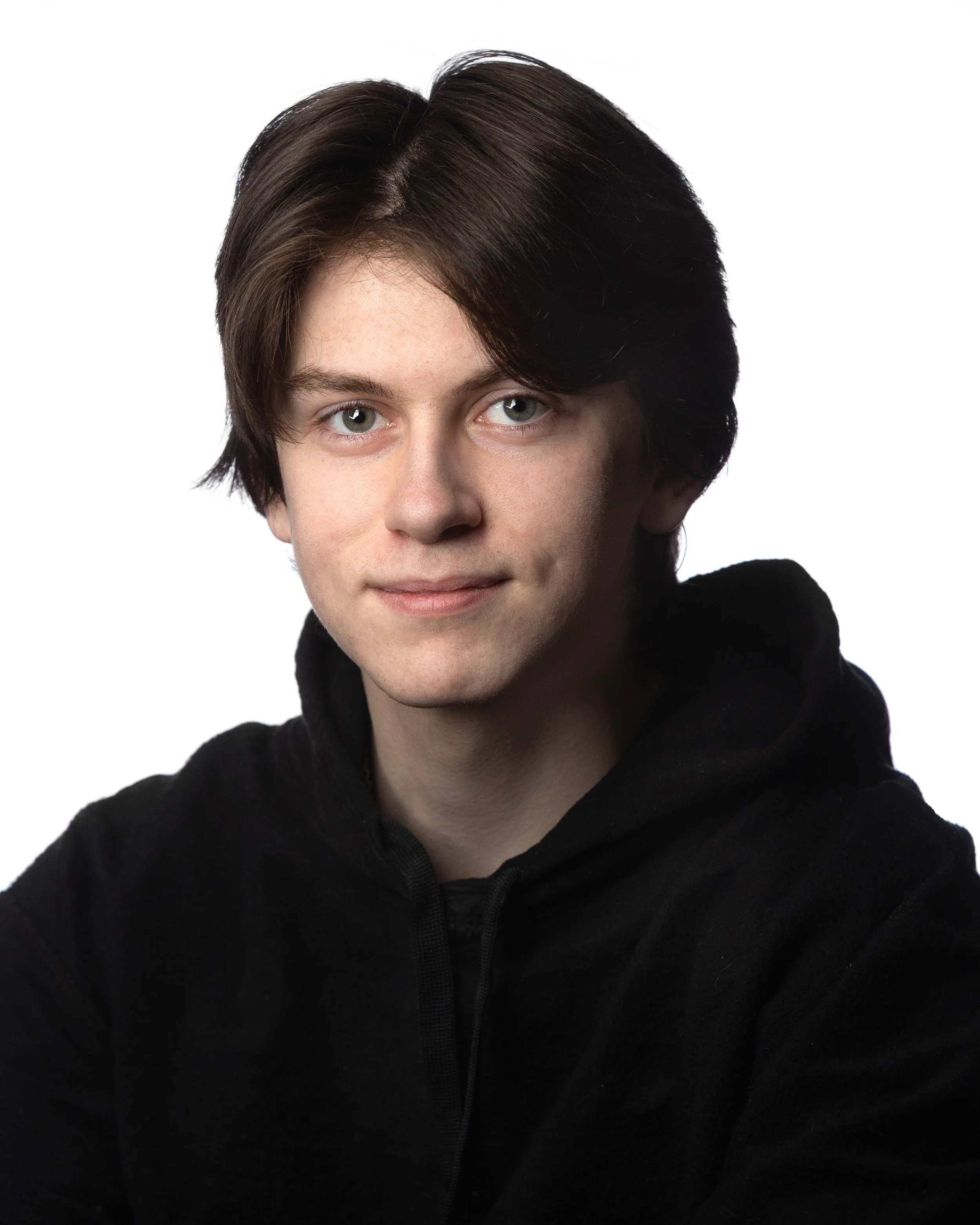 Portrait of a young man with dark brown hair and light blue eyes, wearing a black hoodie, against a white background.