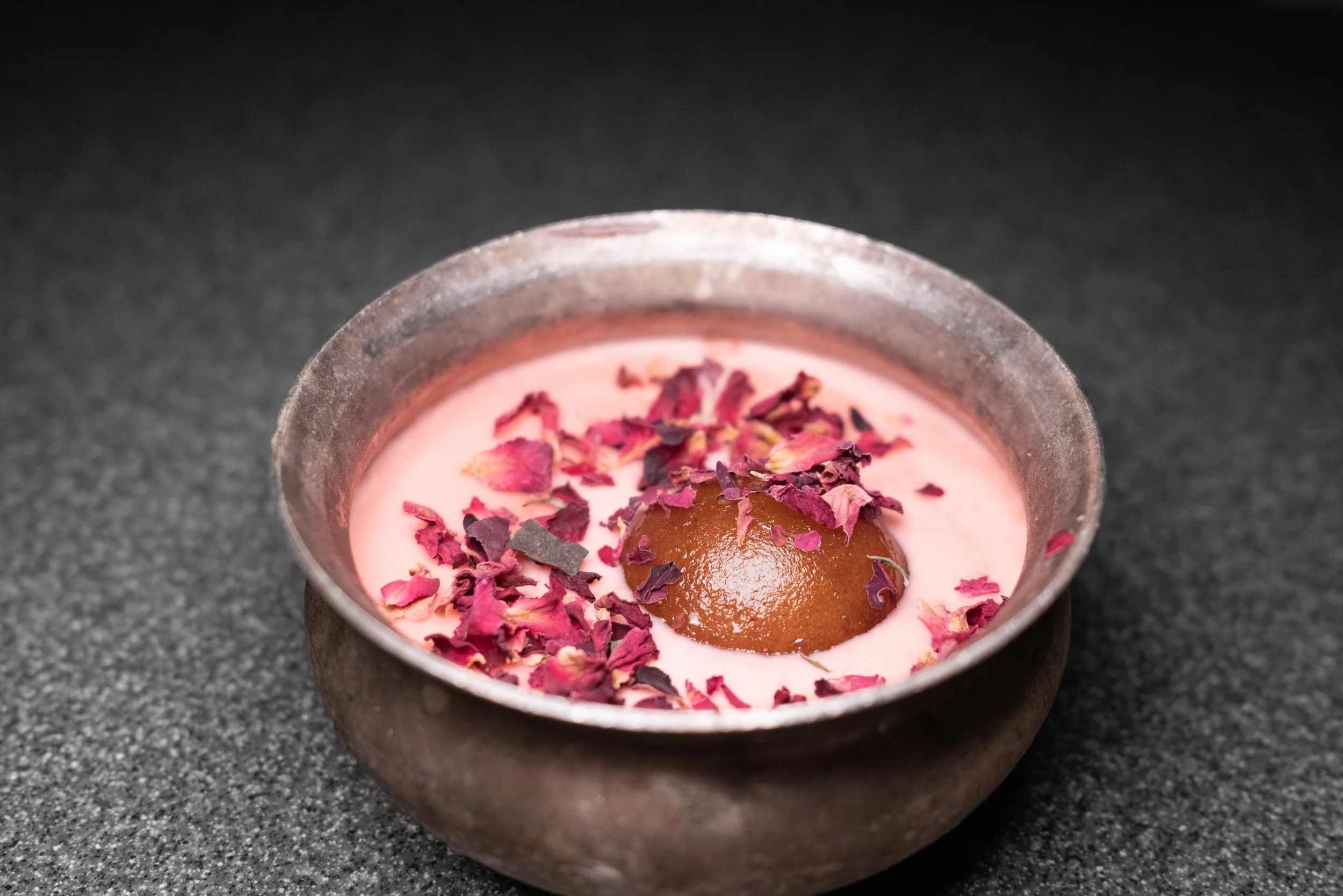 Pink dessert in a rustic bowl topped with dried rose petals and a glazed date.