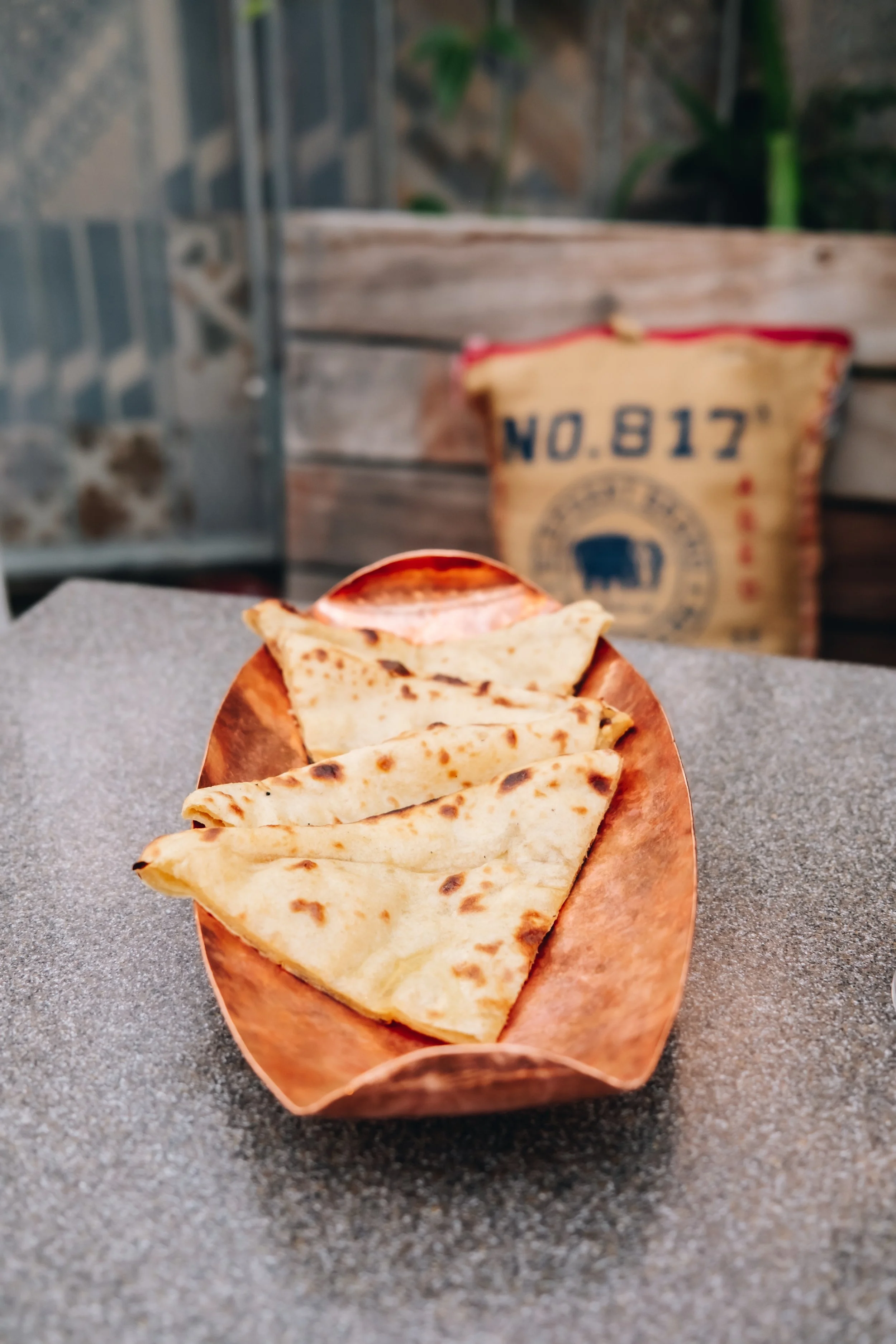 Four pieces of naan bread on a copper plate on a gray table with a blurred background.