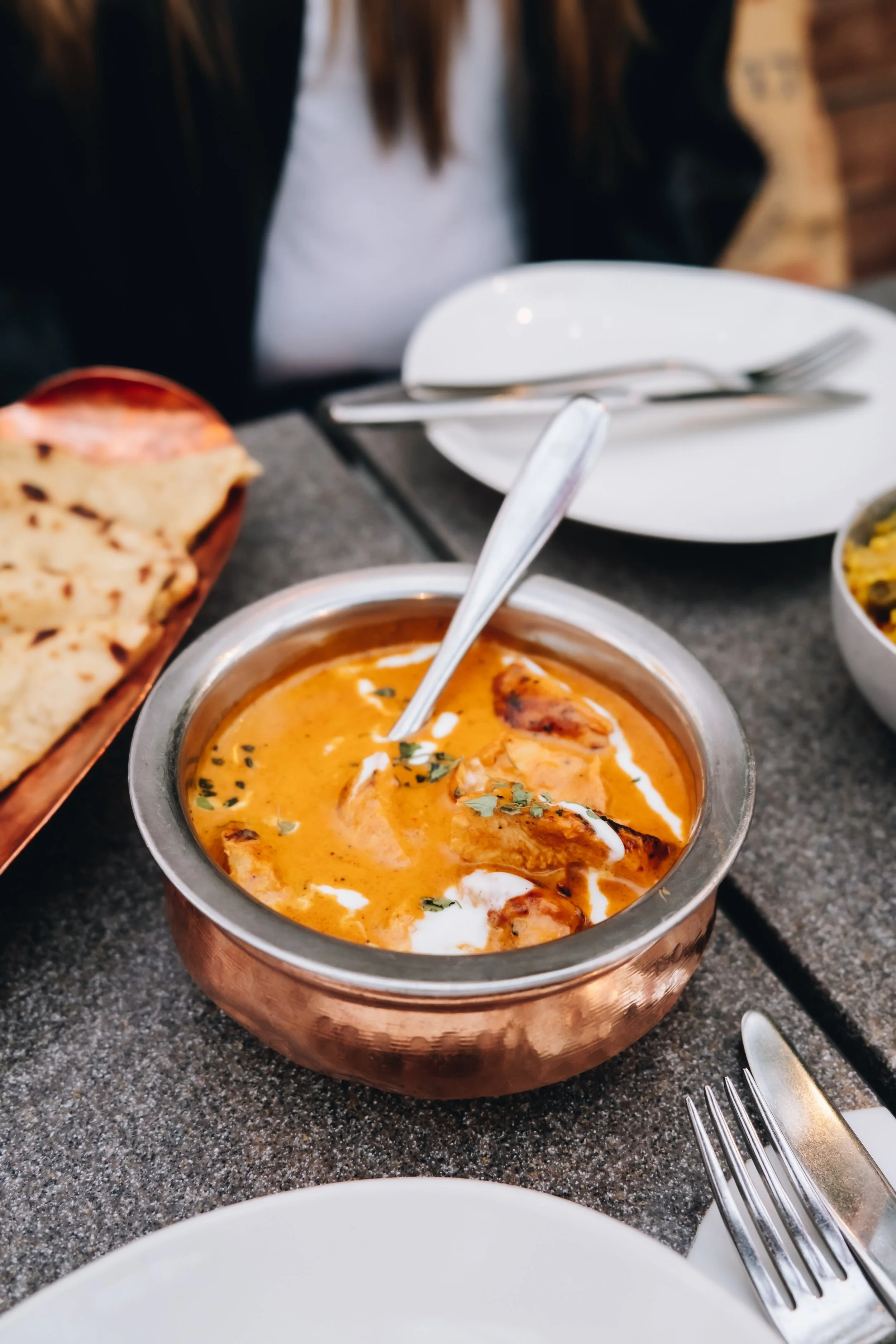 A bowl of Indian butter chicken with a side of naan bread on a gray textured table.
