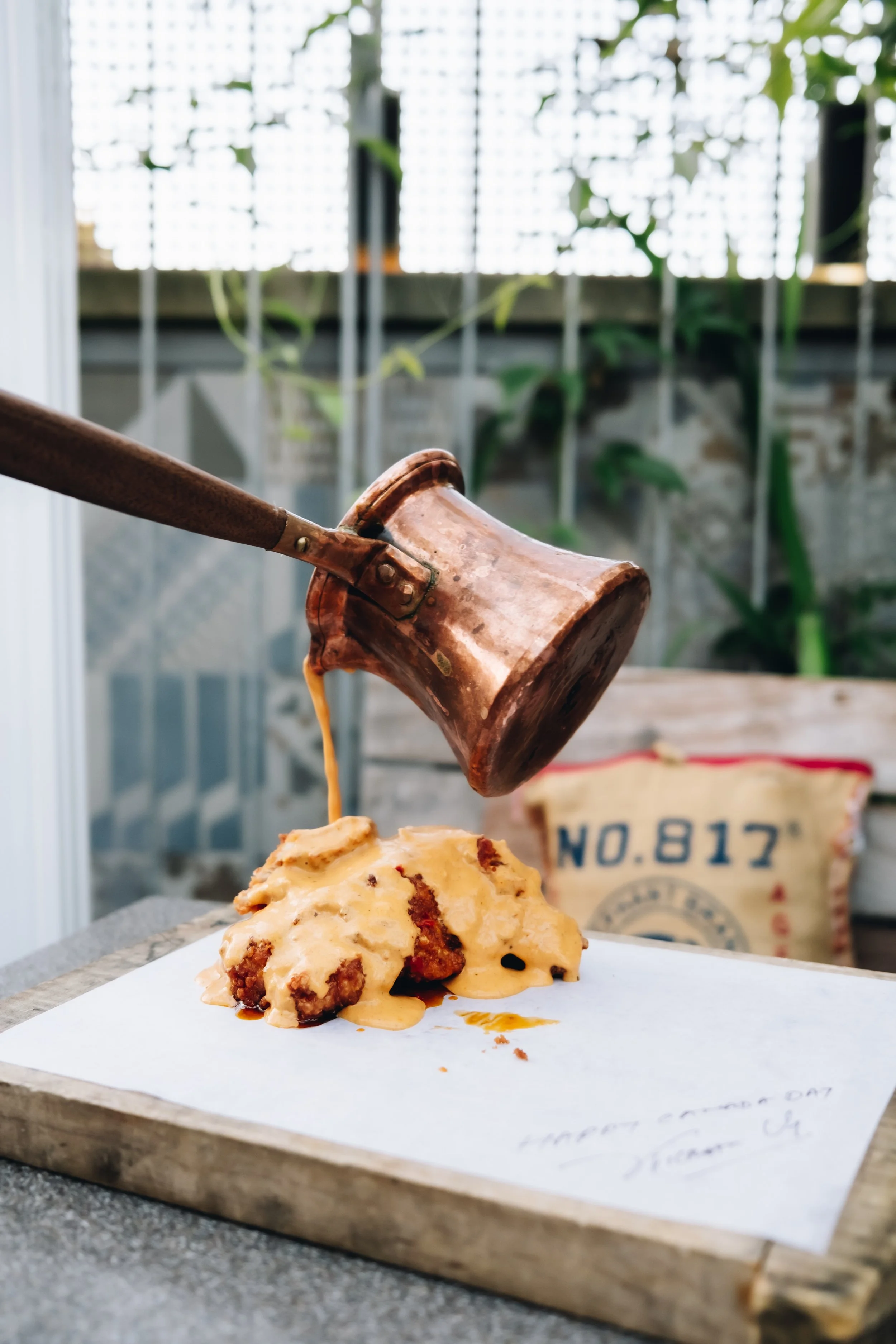 A copper coffee pot pouring hot coffee over a pile of biscuits on a wooden board.