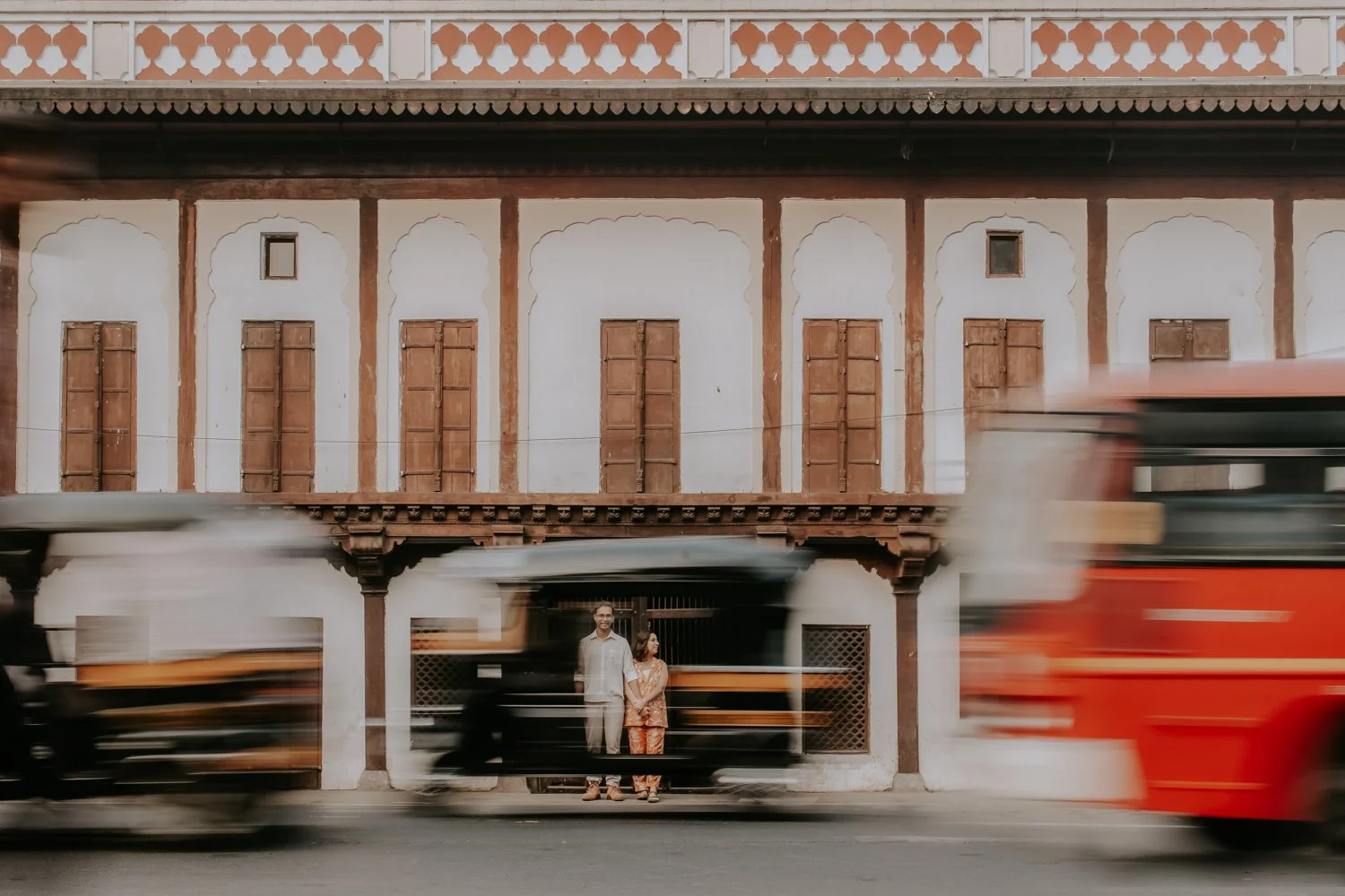 A historic building facade with wooden shutters, blurred traffic in front, and two people standing.