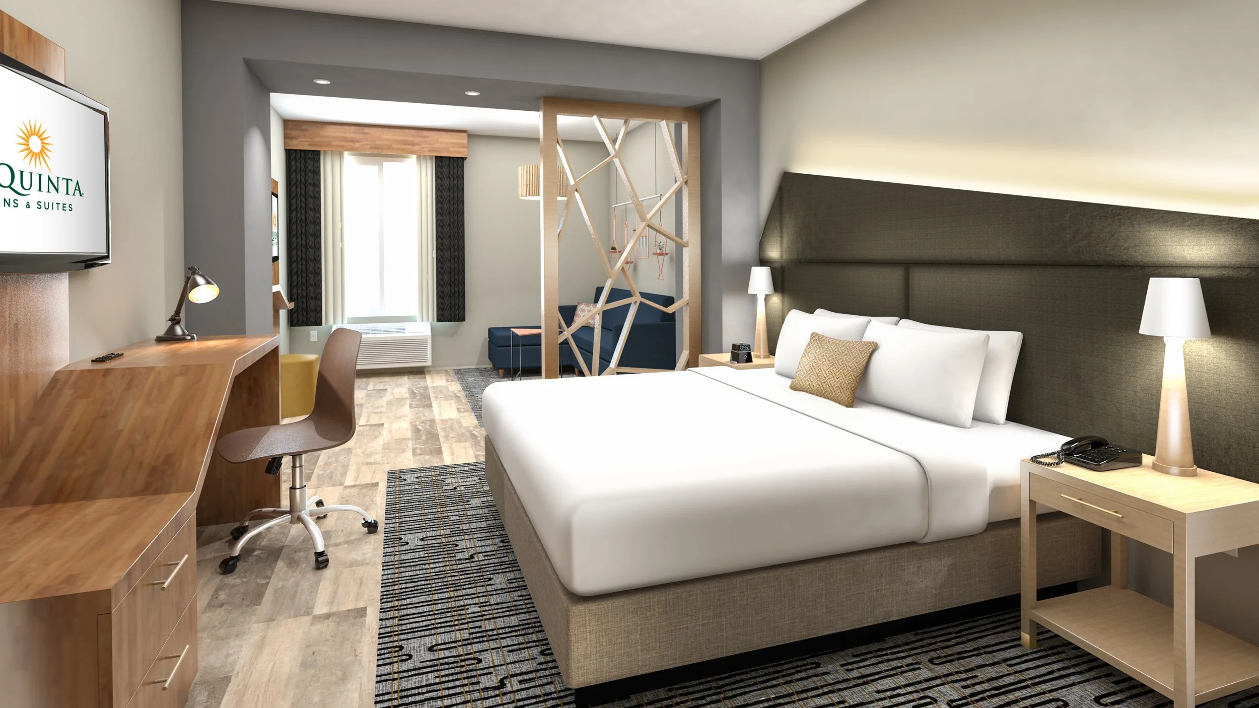 Modern hotel room with a large bed, nightstands, lamps, a desk with a chair, a patterned rug, and a sitting area with a blue sofa near a window.