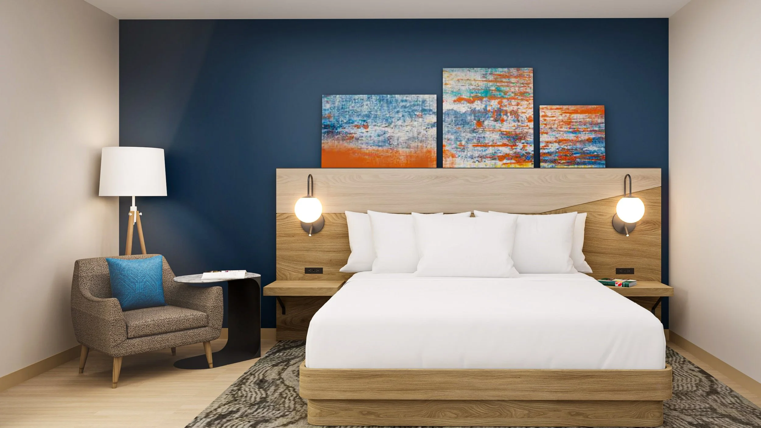 Modern hotel bedroom with a white bed, blue accent wall, and abstract artwork above the headboard. There is a gray armchair with a blue pillow, a floor lamp, and wall-mounted reading lights.
