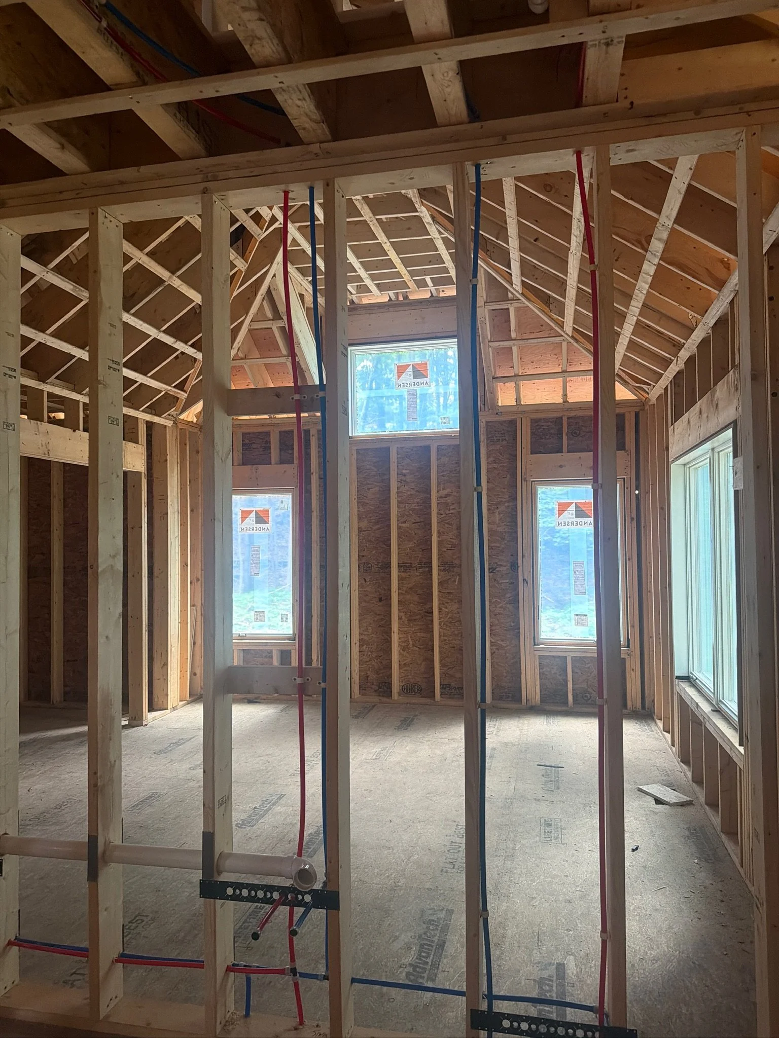 Residential construction progress showing rough-in plumbing PEX lines installed inside framed stud walls with vaulted primary bedroom in the background .