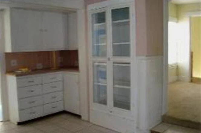 Dated kitched showing circa 1950 cabinets and an space divided by a wall of cabinets.