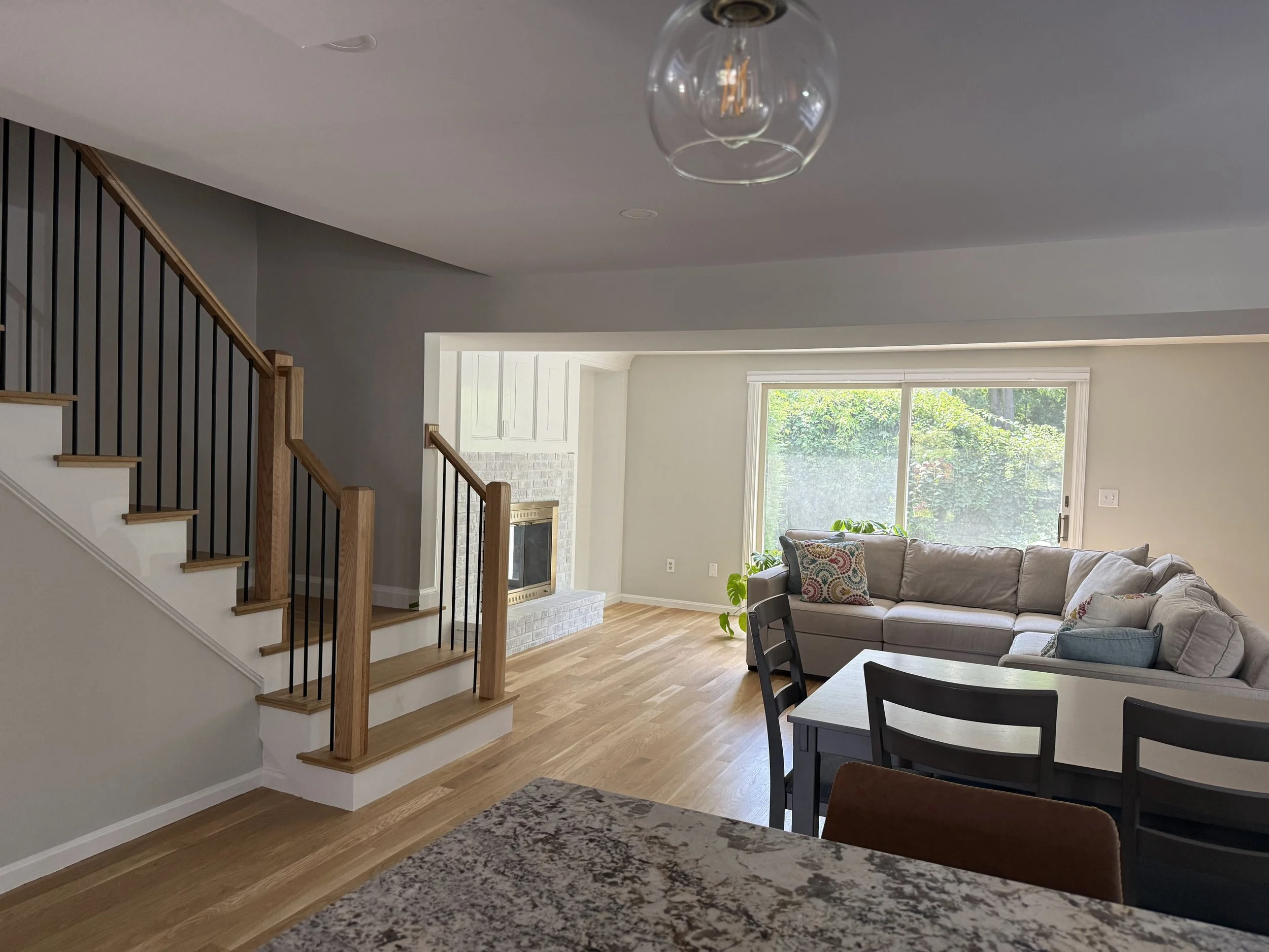 Renovated wooden staircase with modern railings leading down to an open-concept living area featuring a custom fireplace.
