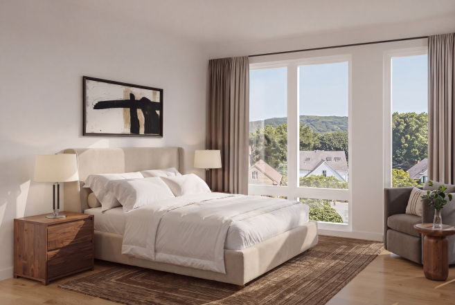Modern bedroom with a large bed, nightstand, lamps, artwork, large window overlooking trees and houses, and a seating area with a small table and plant.
